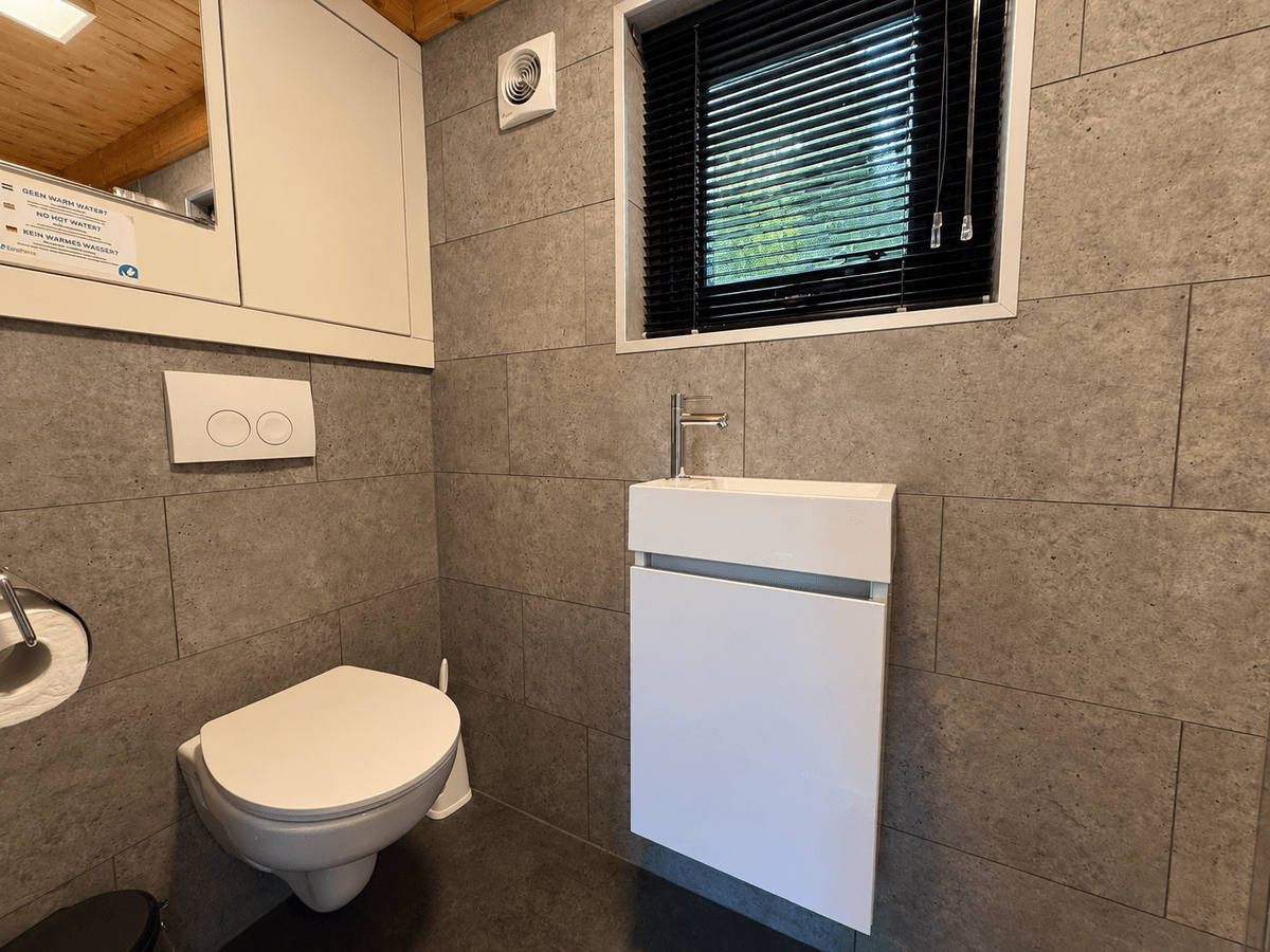 Modern toilet met wandmeubel en kleine venster met zwarte jaloezieën in een betegelde ruimte