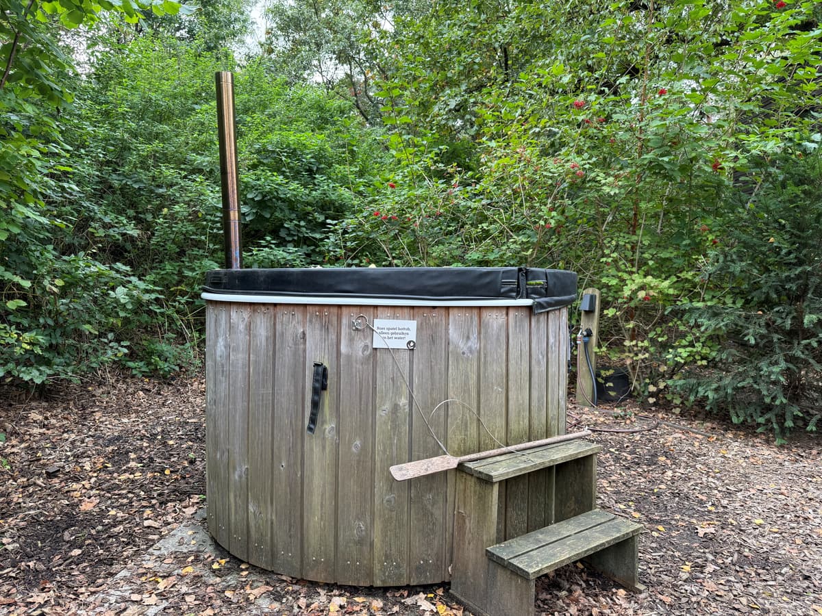 Houten hot tub omgeven door bomen en struiken met een trapje aan de voorkant.