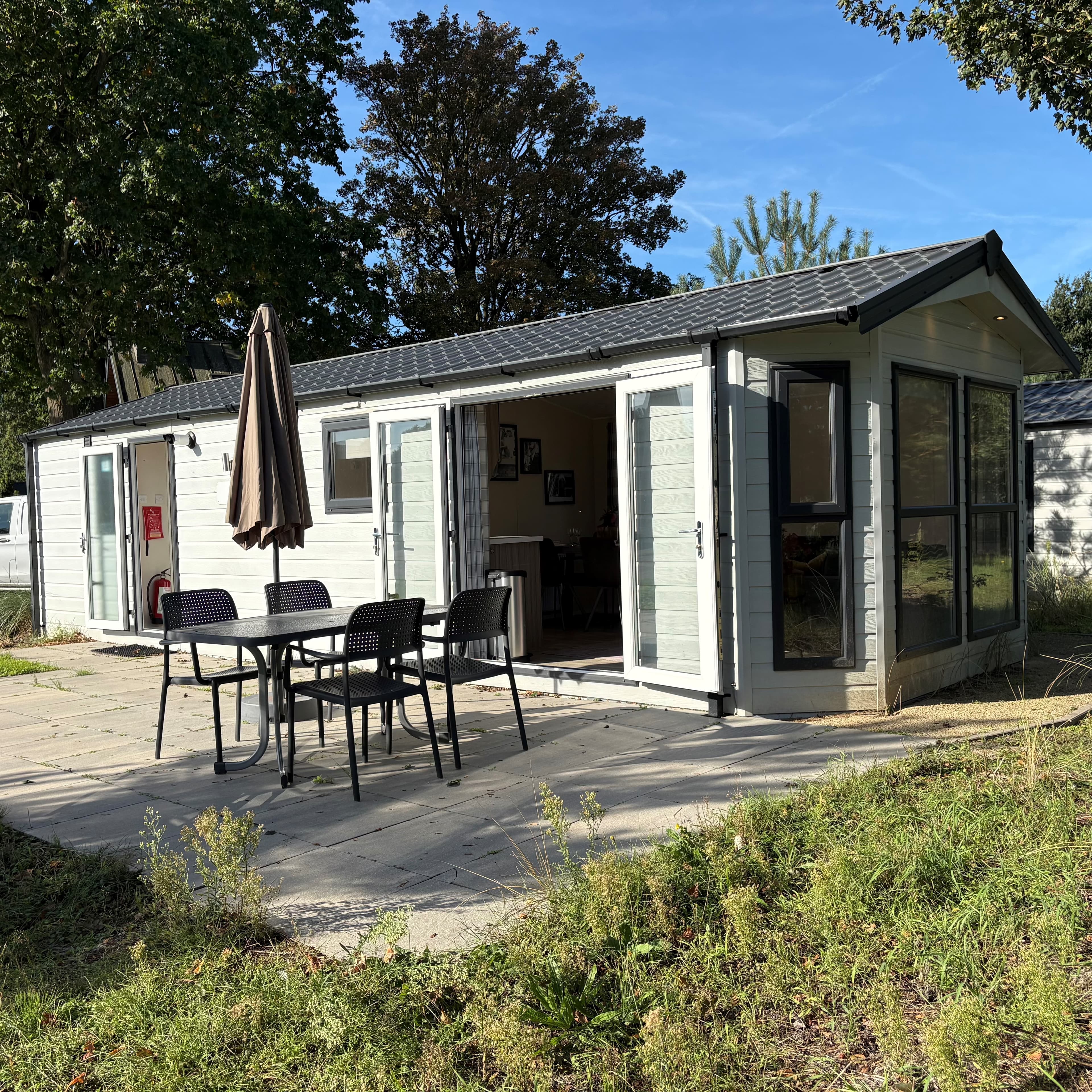 Recreatiewoning met terras en tuinmeubilair, omgeven door bomen en gras op EuroParcs Zuiderzee.