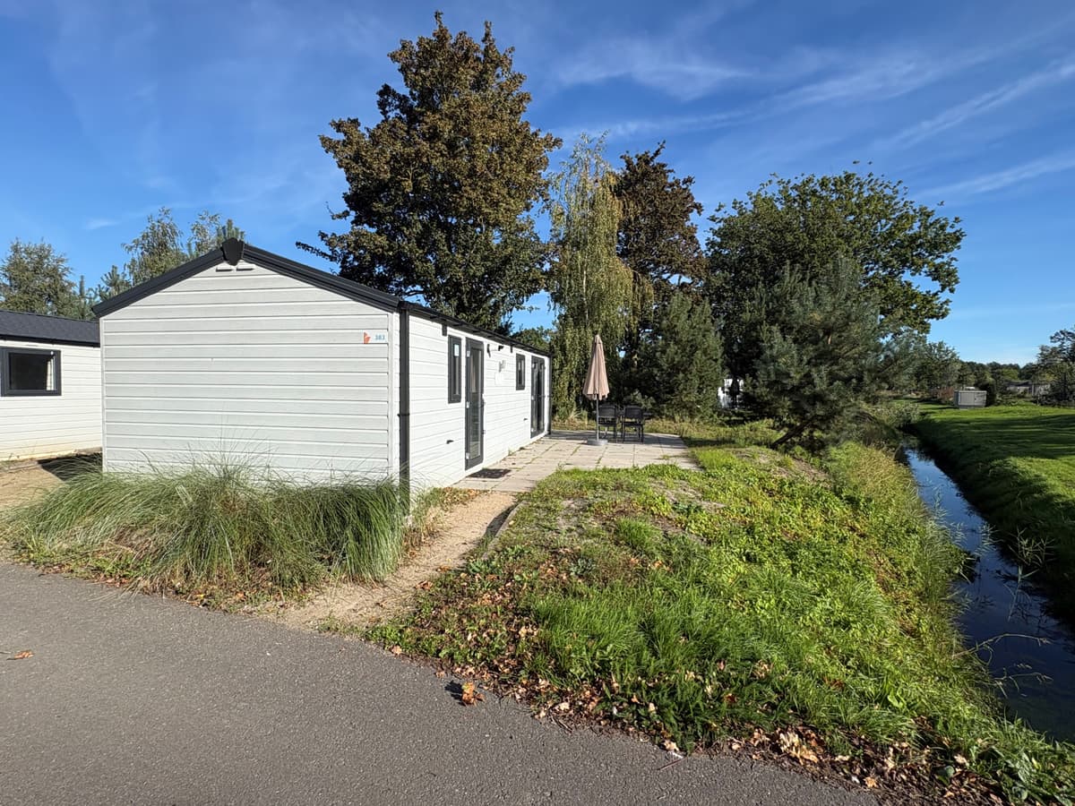 Recreatiewoning met terras en parasol, omgeven door groen en waterpartij, gelegen in EuroParcs Zuiderzee.