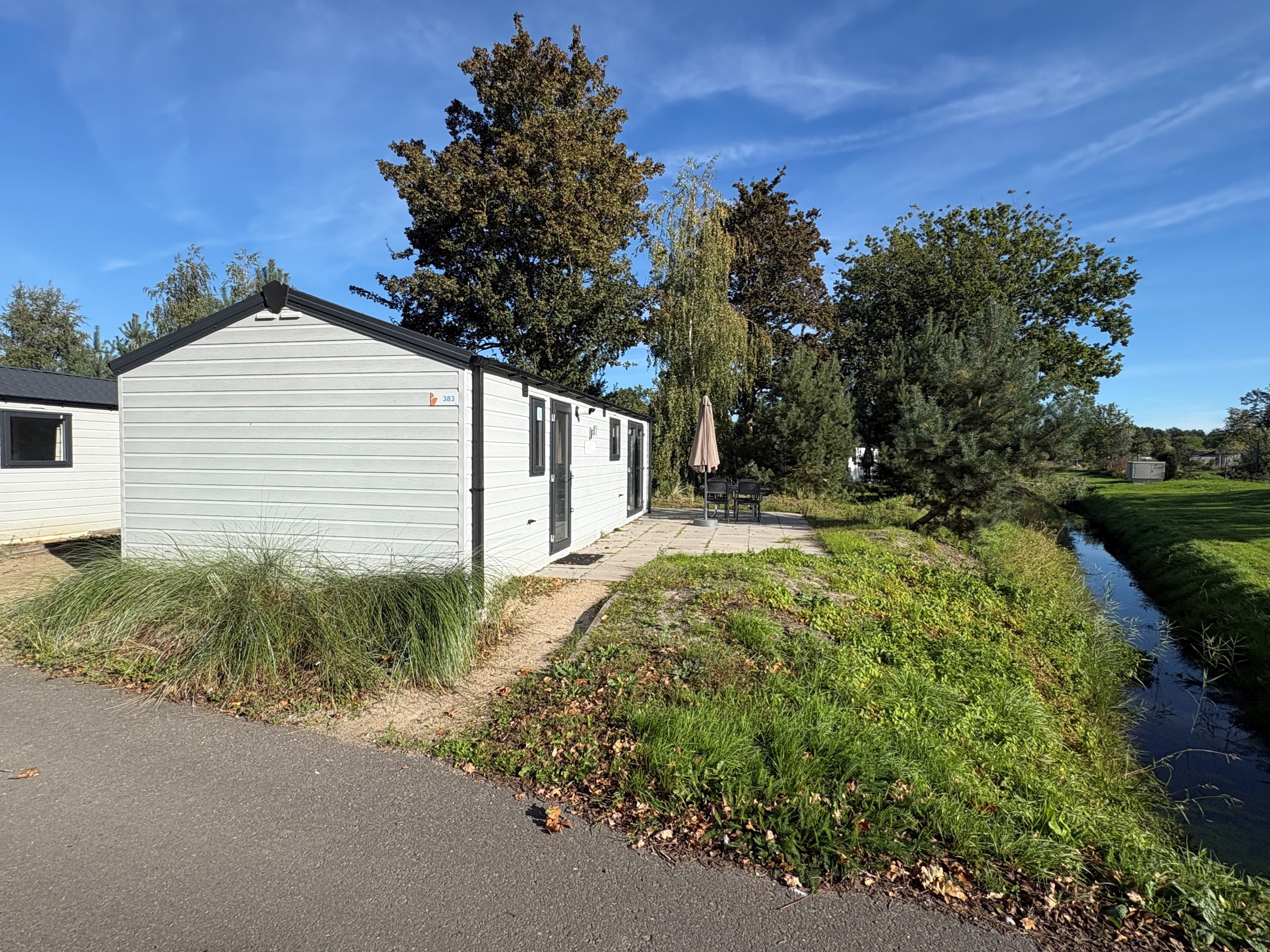 Recreatiewoning met terras en parasol, omgeven door groen en waterpartij, gelegen in EuroParcs Zuiderzee.