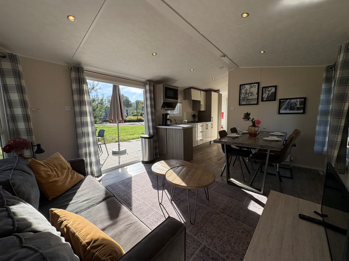 Moderne recreatiewoning met woonkamer, open keuken en toegang tot buiten met tuinmeubelen en parasol.