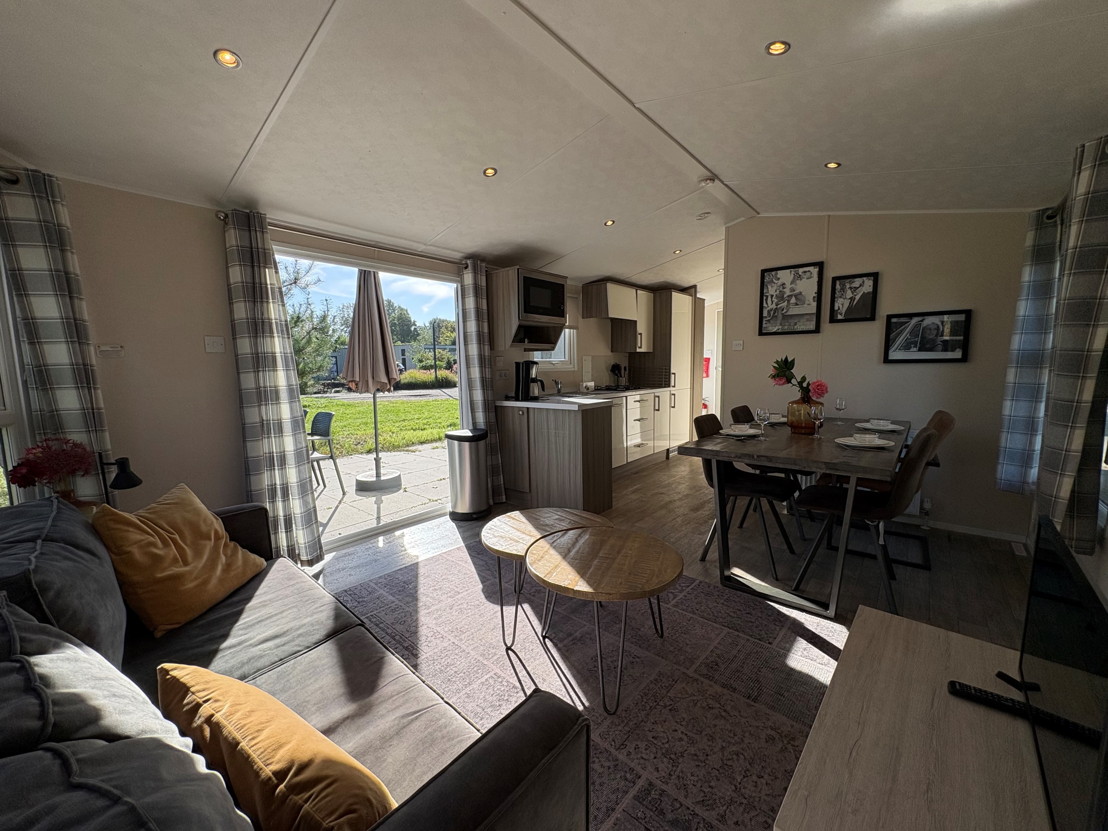 Moderne recreatiewoning met woonkamer, open keuken en toegang tot buiten met tuinmeubelen en parasol.