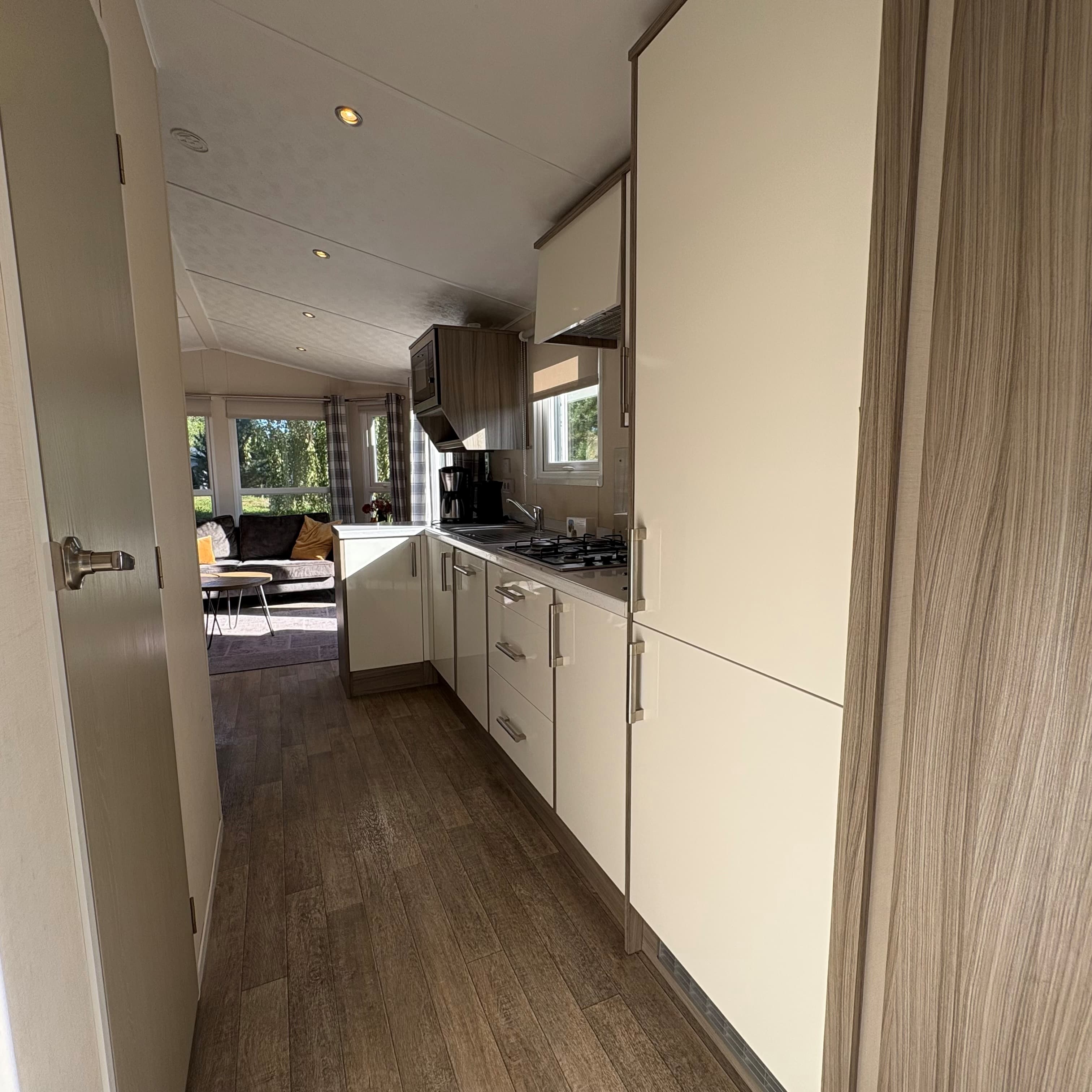 Gangen in de recreatiewoning met lichte kasten en een keuken met gasfornuis en een raam voor natuurlijk licht