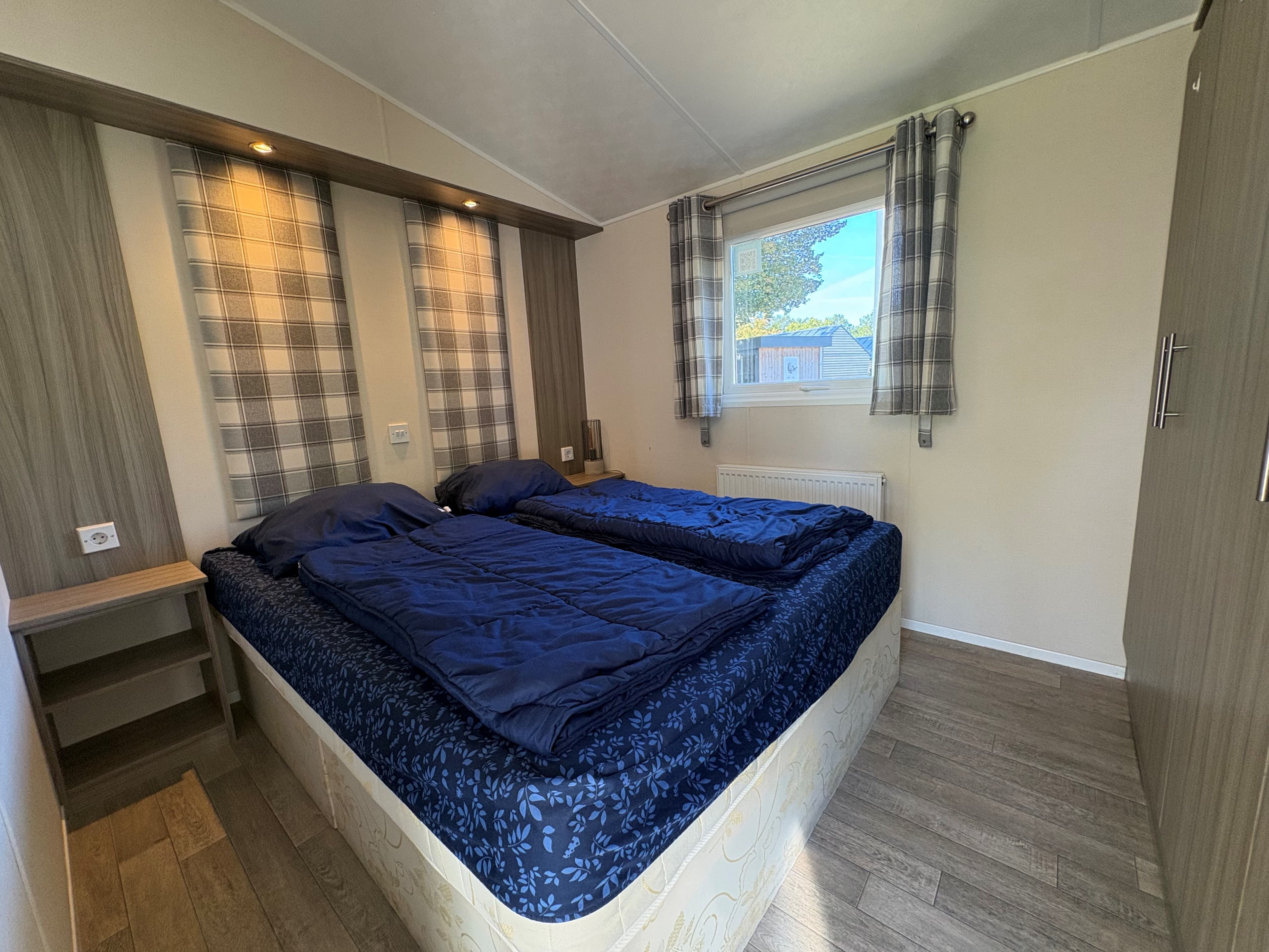 Slaapkamer met twee eenpersoonsbedden, gordijnen en wandverlichting in een recreatiewoning.
