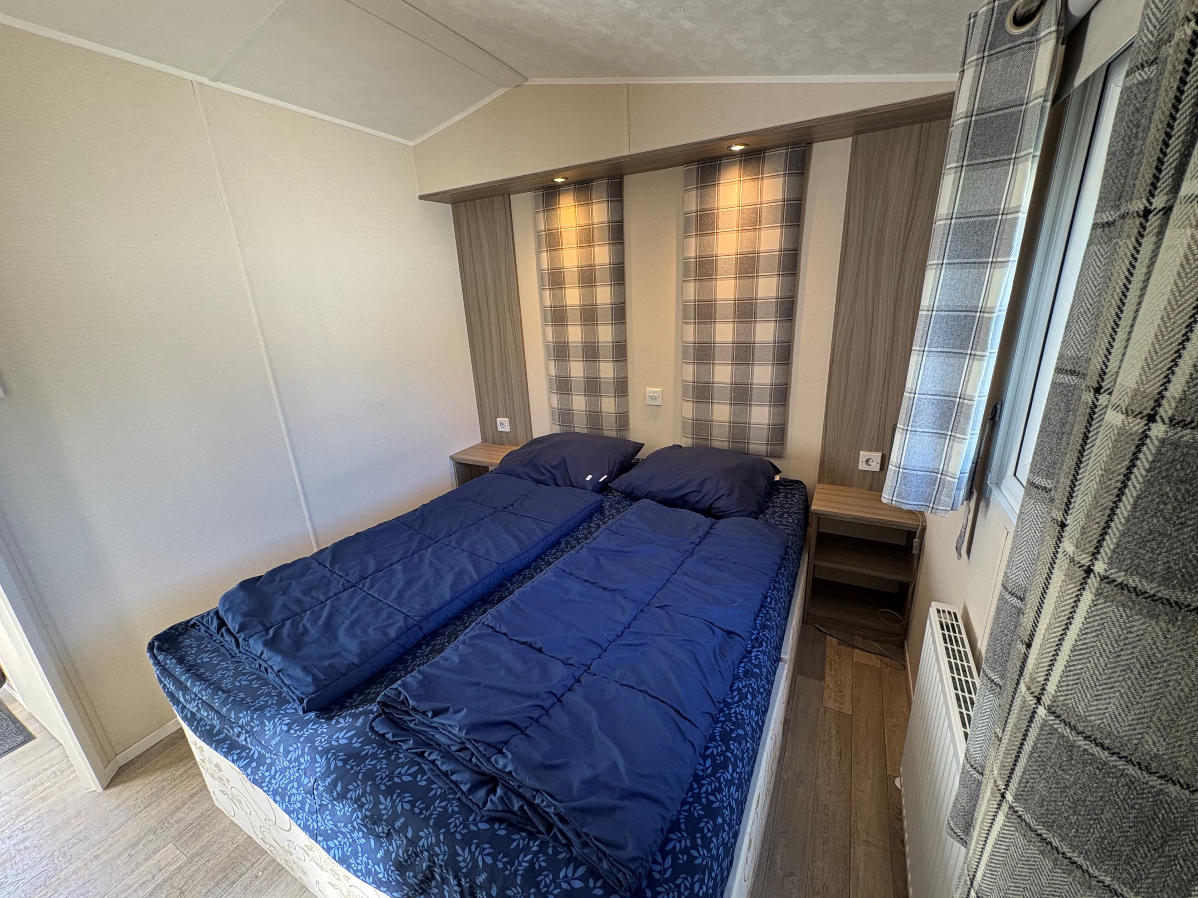 Slaapkamer met twee losse bedden, nachtkastjes en wandverlichting in een recreatiewoning.