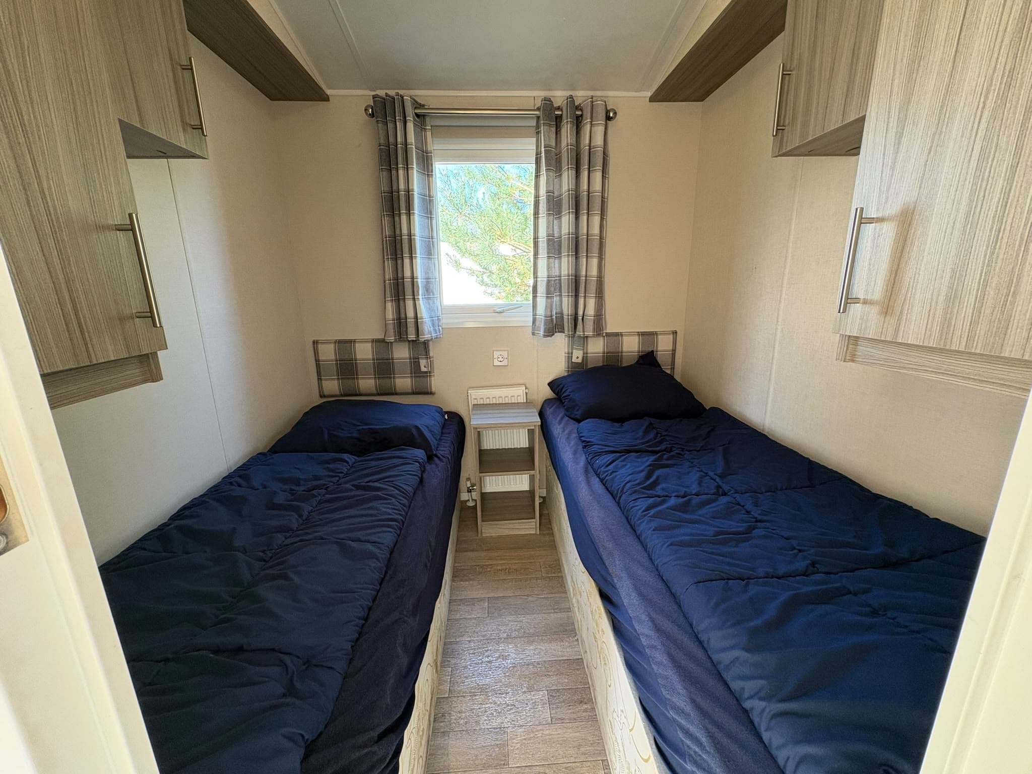Slaapkamer met twee eenpersoonsbedden en ramen met vitrage in neutrale kleurstellingen