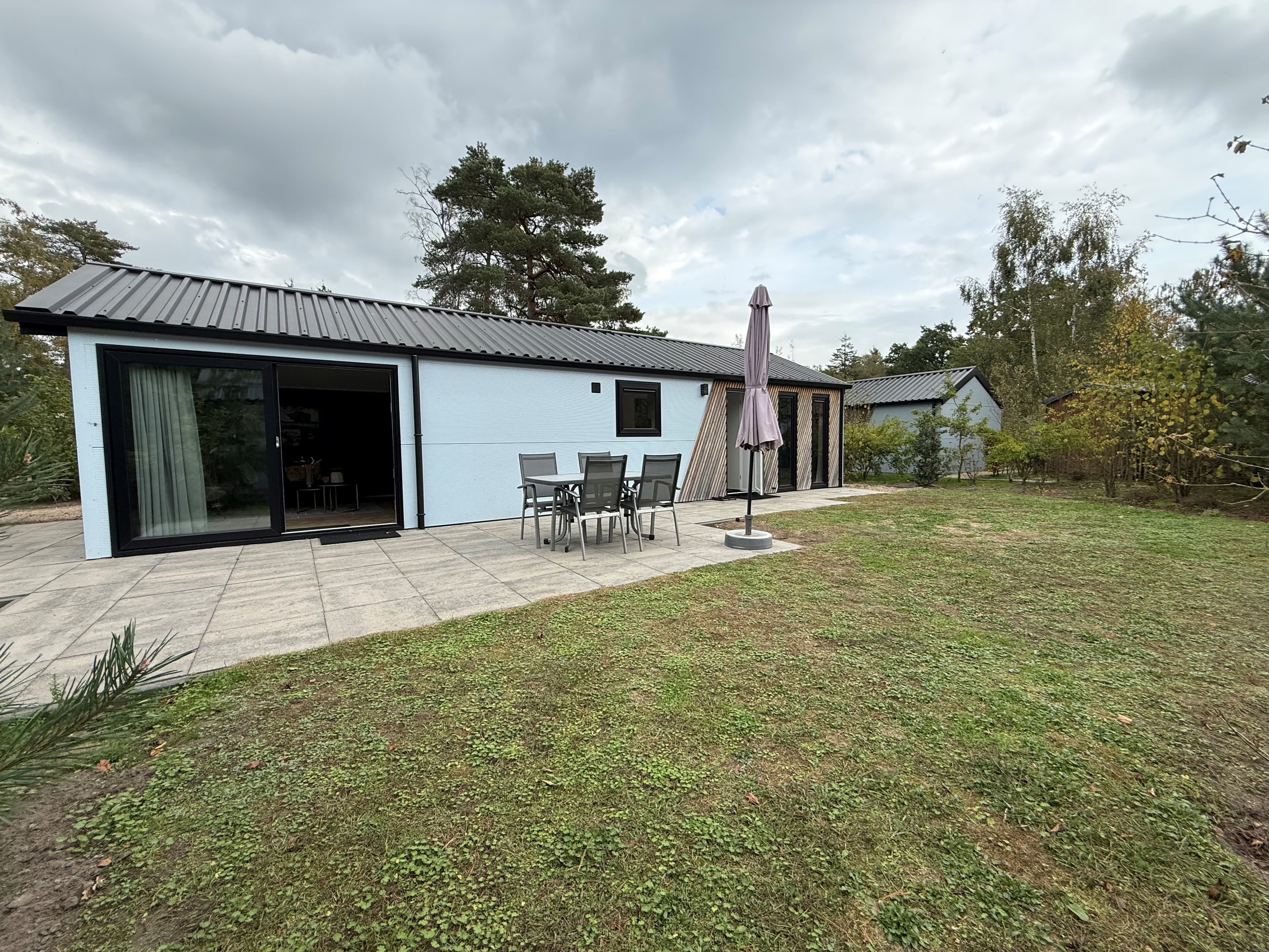 Moderne recreatiewoning met tuin en terrassen, zicht op groen en bomen, en een parasol bij de zithoek buiten