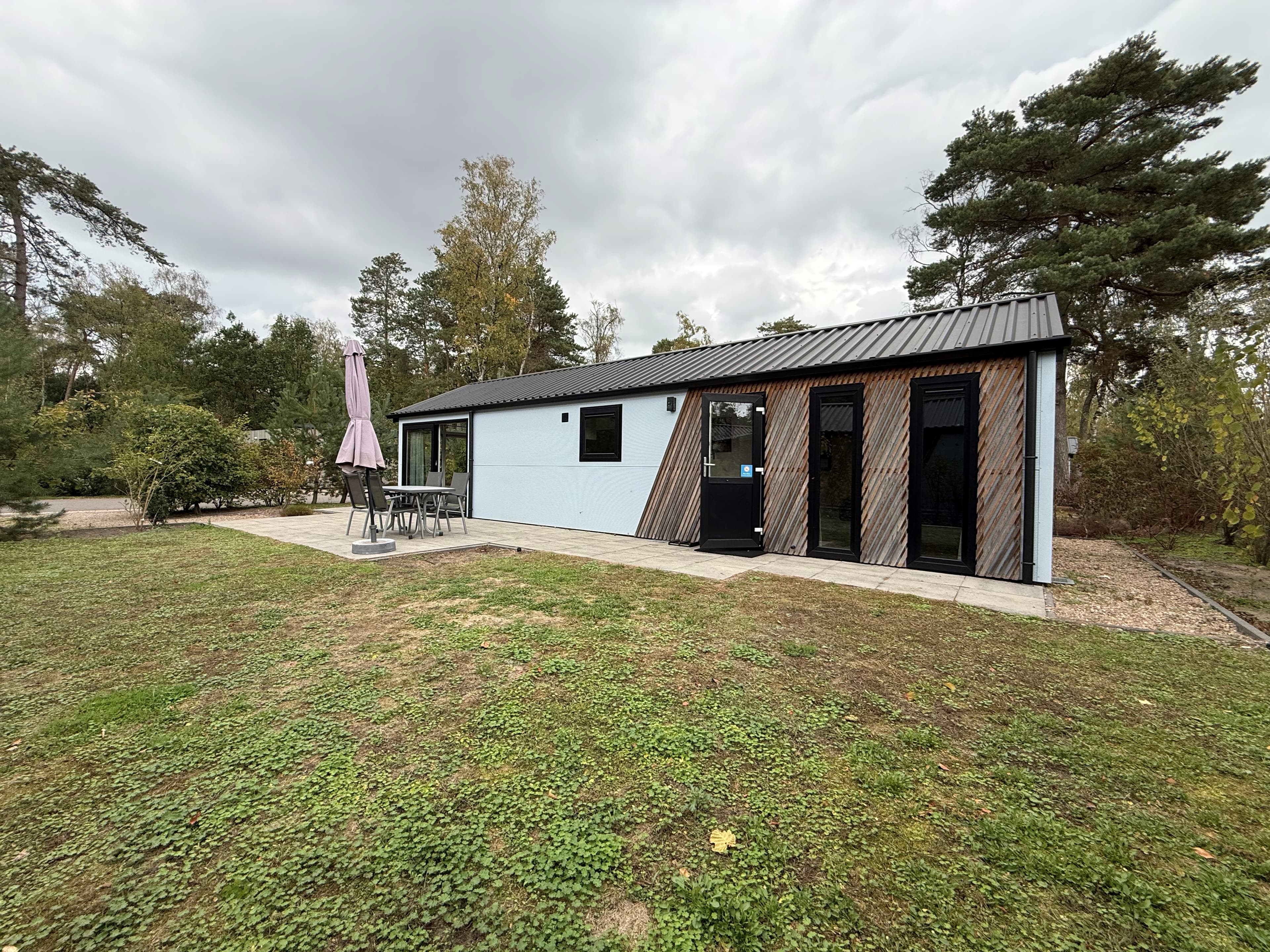 Recreatiewoning met een moderne uitstraling, voorzien van een terras met tafel en stoelen, omgeven door gras en bomen.
