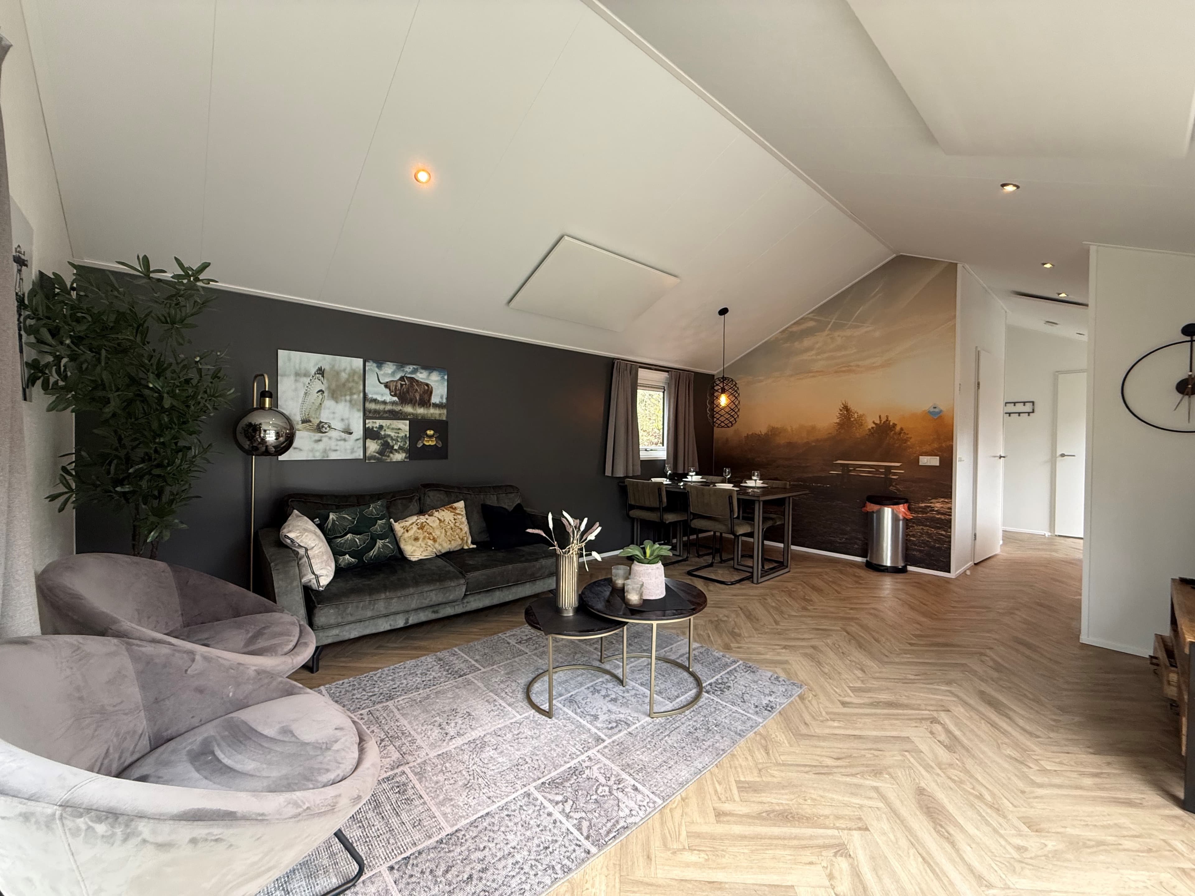Modern interieur van een recreatiewoning met zitgedeelte, eettafel en natuurdecoratie op de muur.