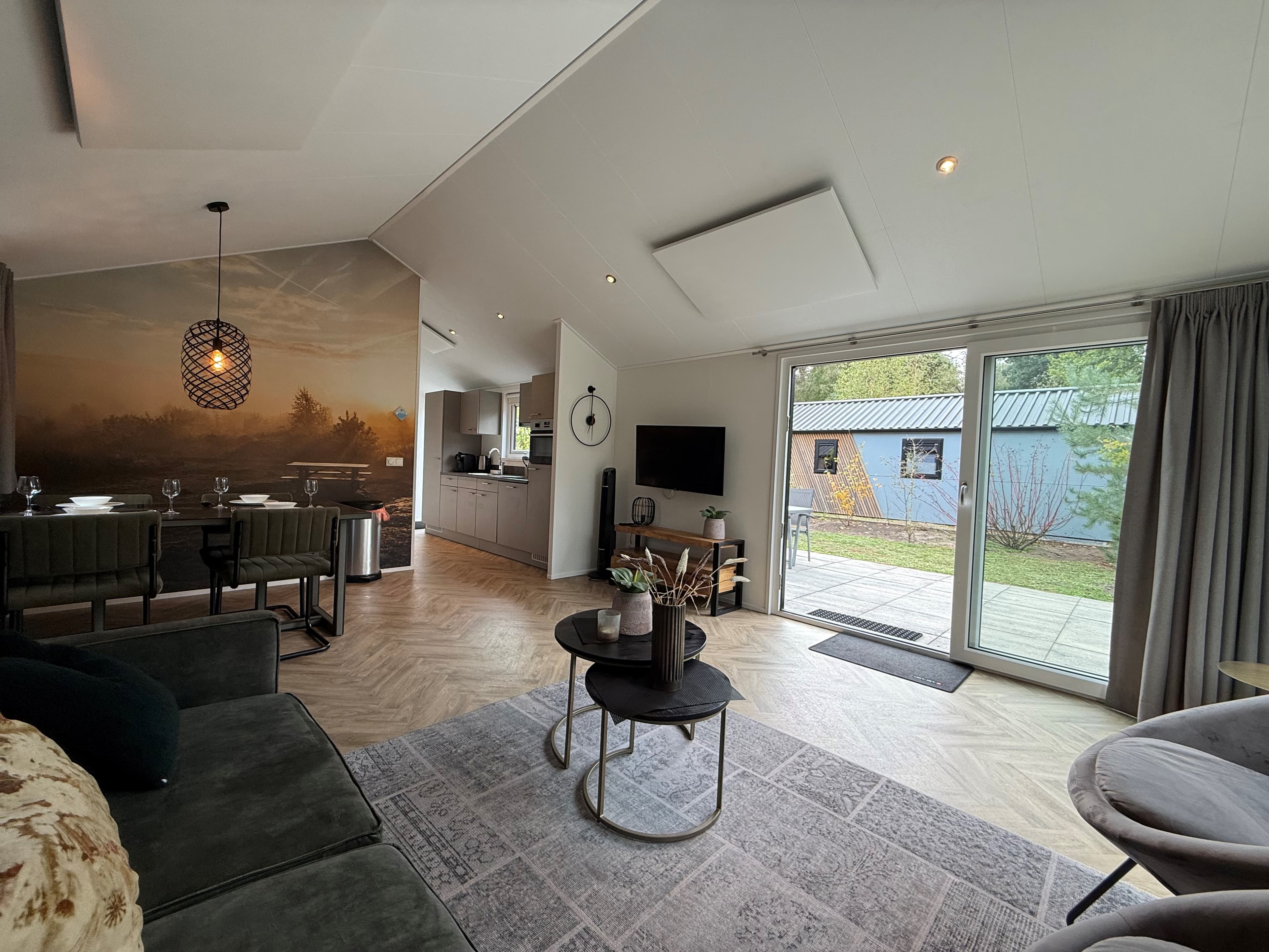 Ruime woonkamer met groene bank, eettafel en toegang tot een buitenpatio met tuinzicht. Moderne inrichting en sfeervolle deta