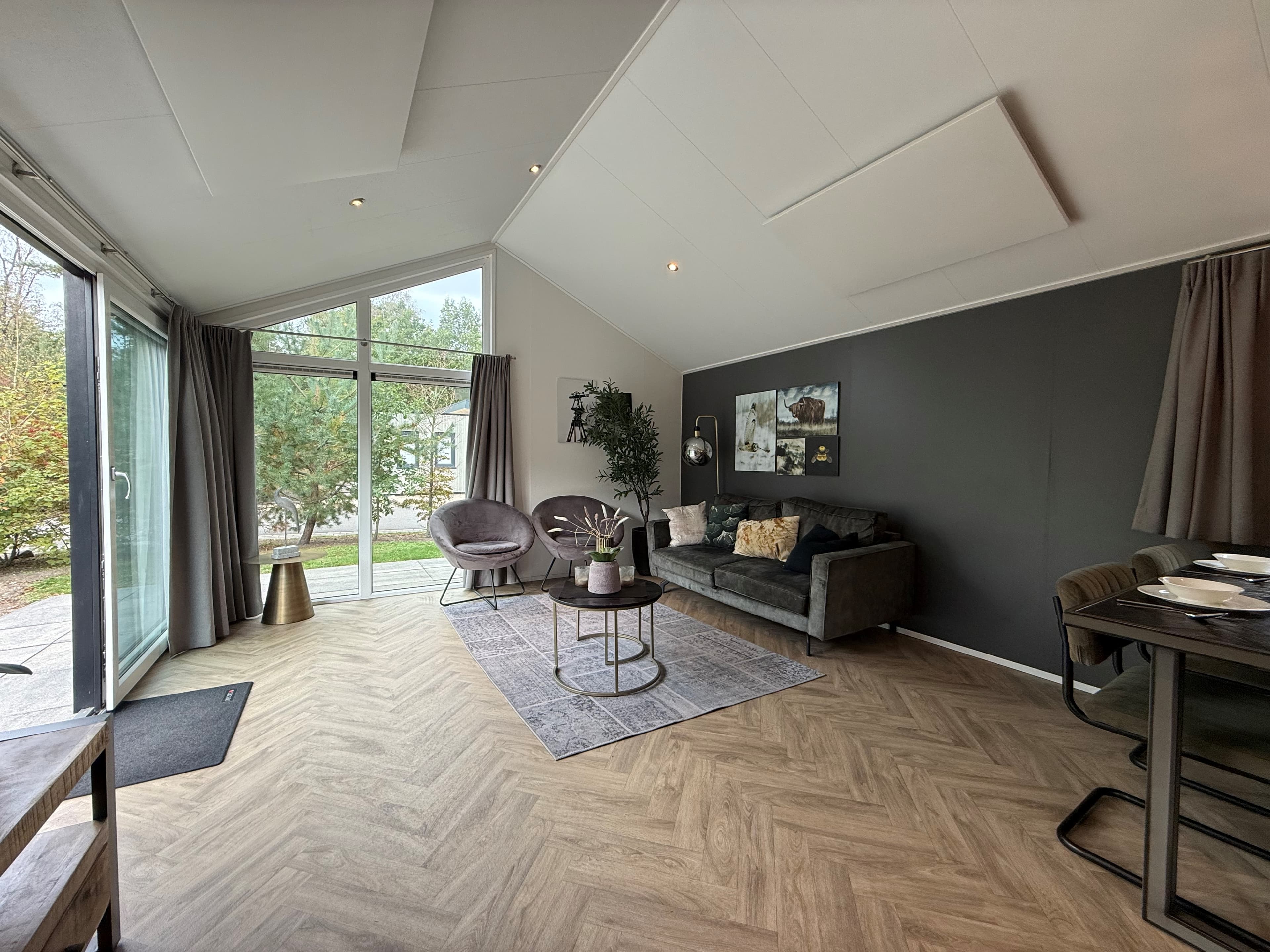 Moderne woonkamer met grote ramen, bank, eetgedeelte en natuurlijke decoratie in een recreatiewoning.