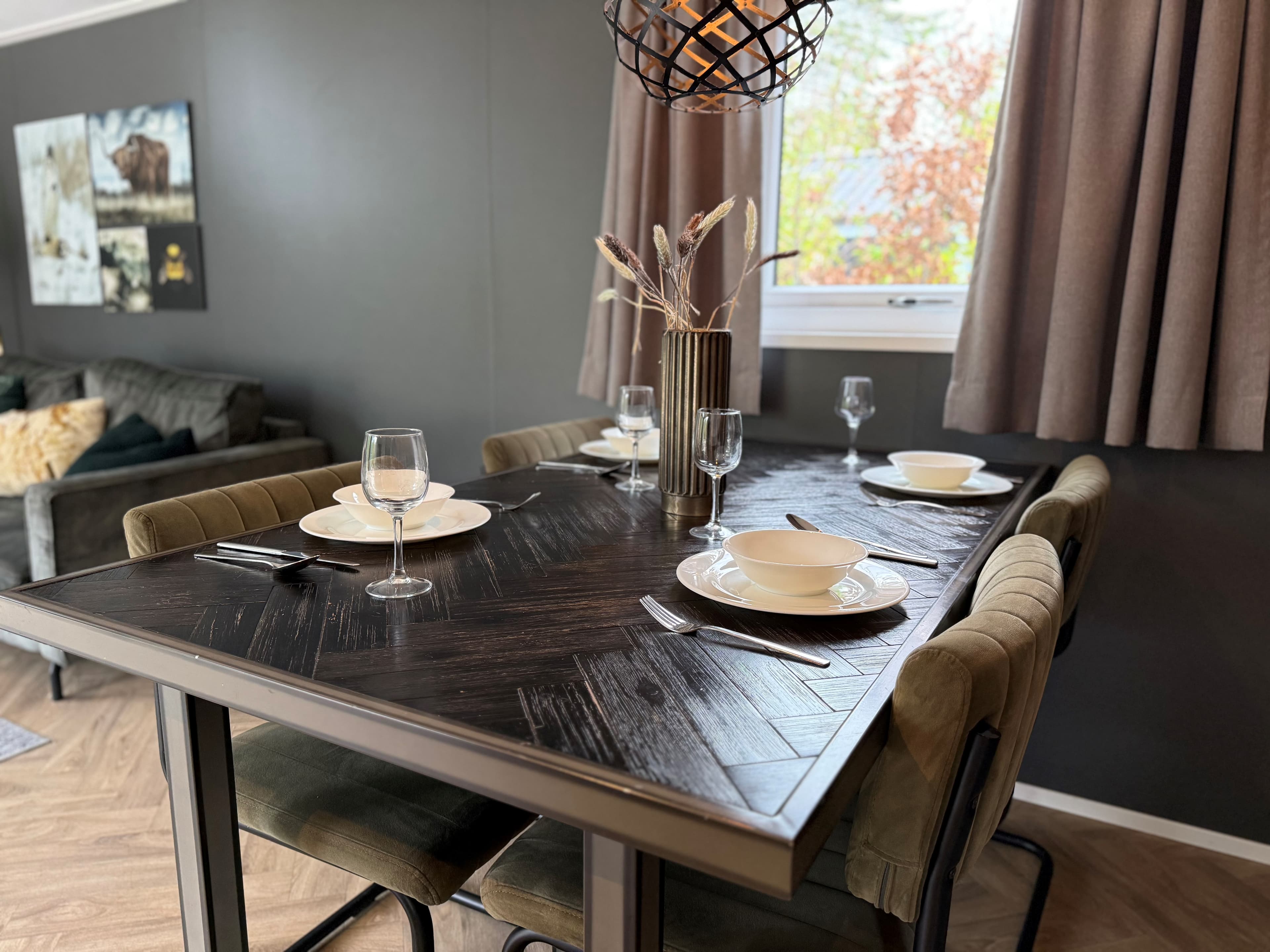 Eettafel met servies en glazen, omringd door stoelen in een stijlvolle woonkamer met kunst aan de muur