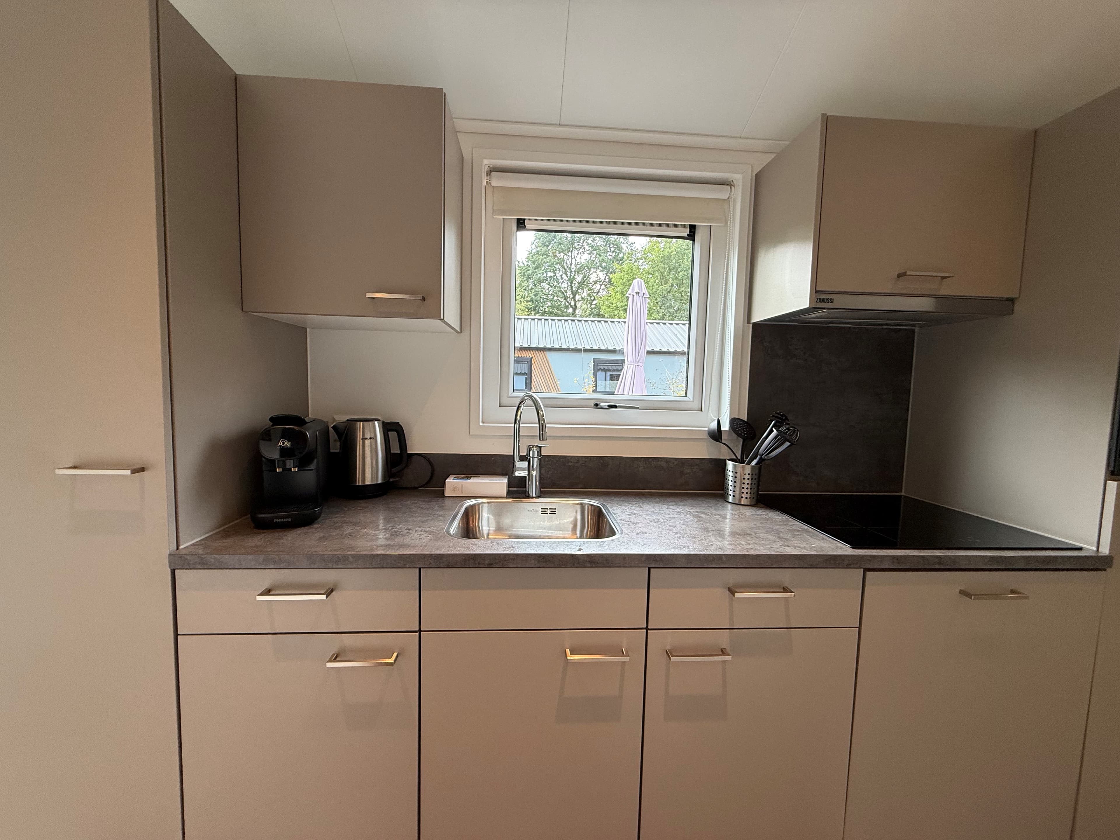 Keukenruimte met moderne kasten, een aanrecht met spoelbak, koffiezetapparaat en uitzicht op een buitenruimte.
