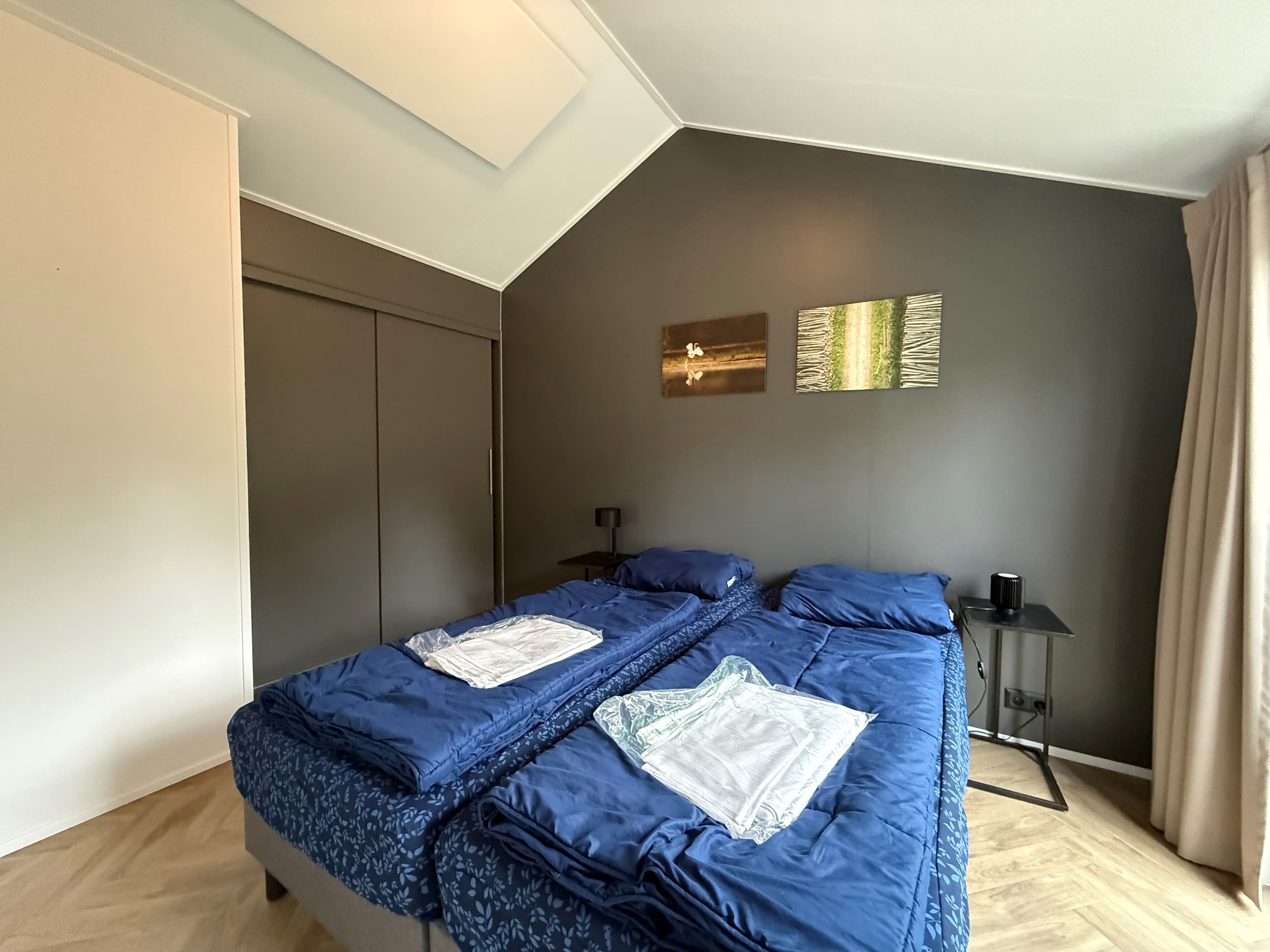 Tweepersoons slaapkamer met twee losse bedden, houten vloeren en donkere muren, voorzien van kunst aan de muur en een nachtka