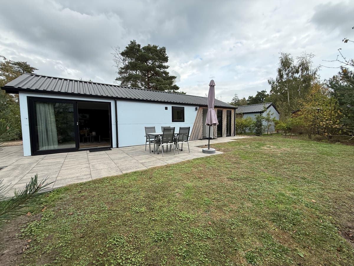 Moderne recreatiewoning met tuin en terrassen, zicht op groen en bomen, en een parasol bij de zithoek buiten