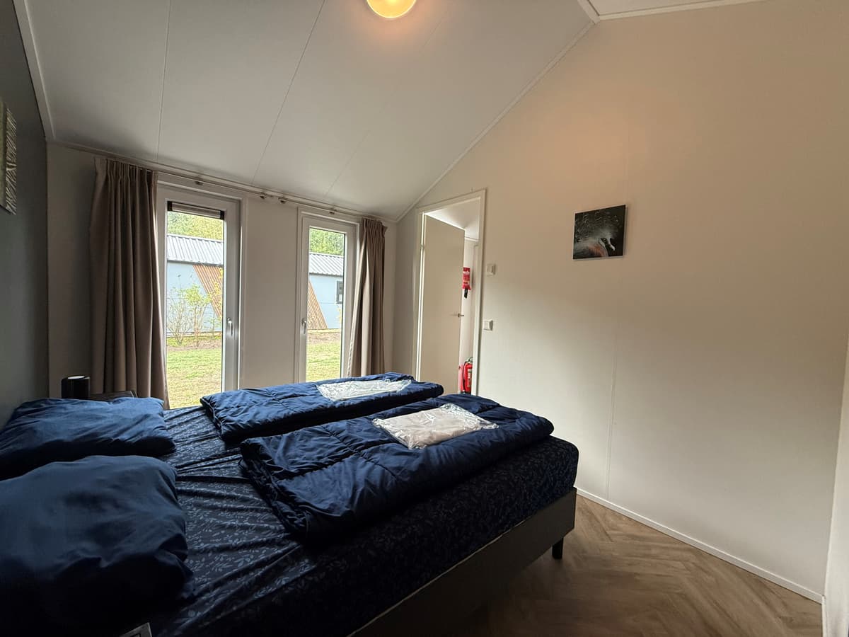 Slaapkamer met twee aparte bedden, ramen met uitzicht op de buitenruimte en een neutrale inrichting