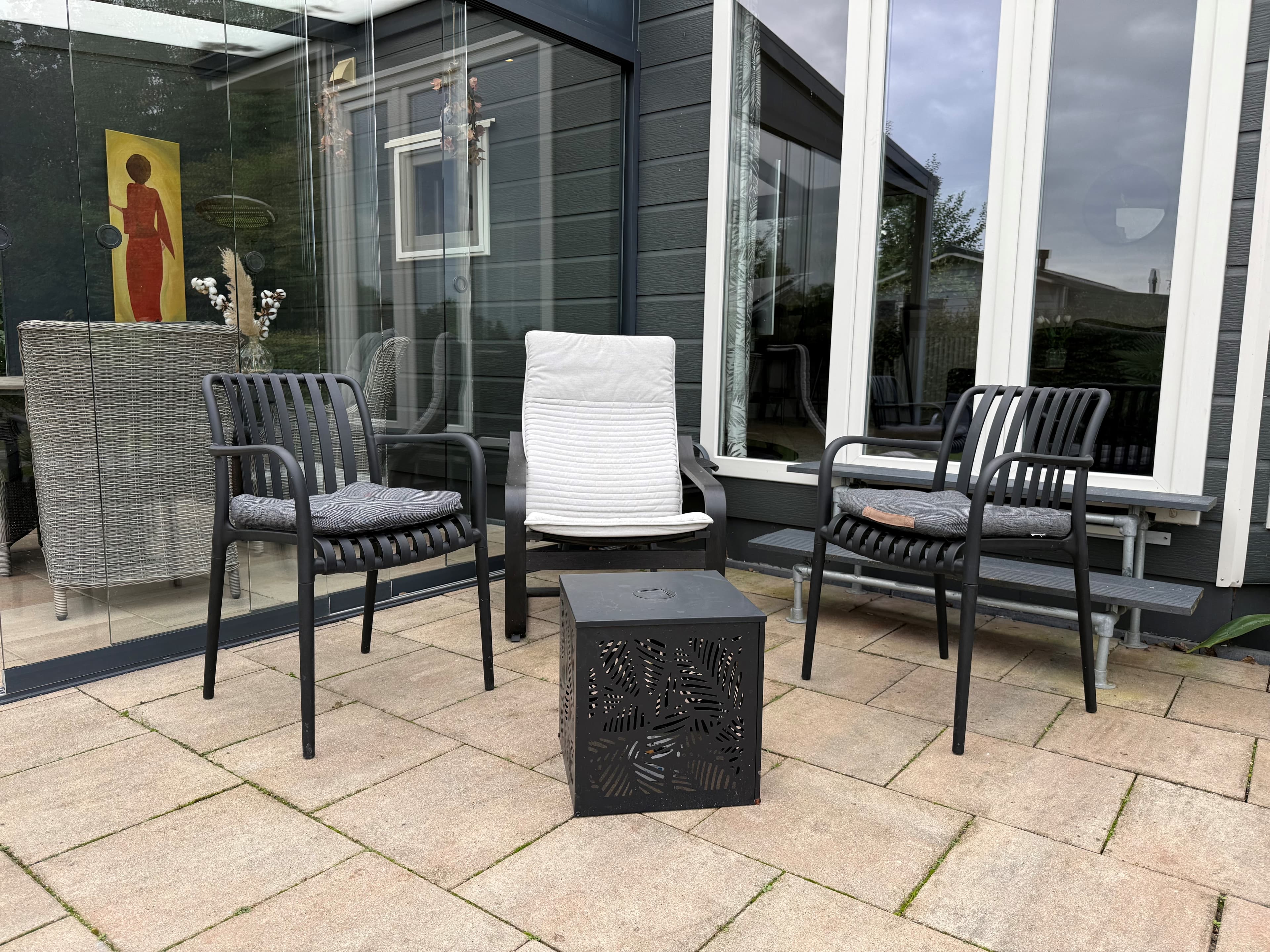 Terras met drie stoelen en een salontafel op een betegelde vloer, omringd door grote ramen van de recreatiewoning