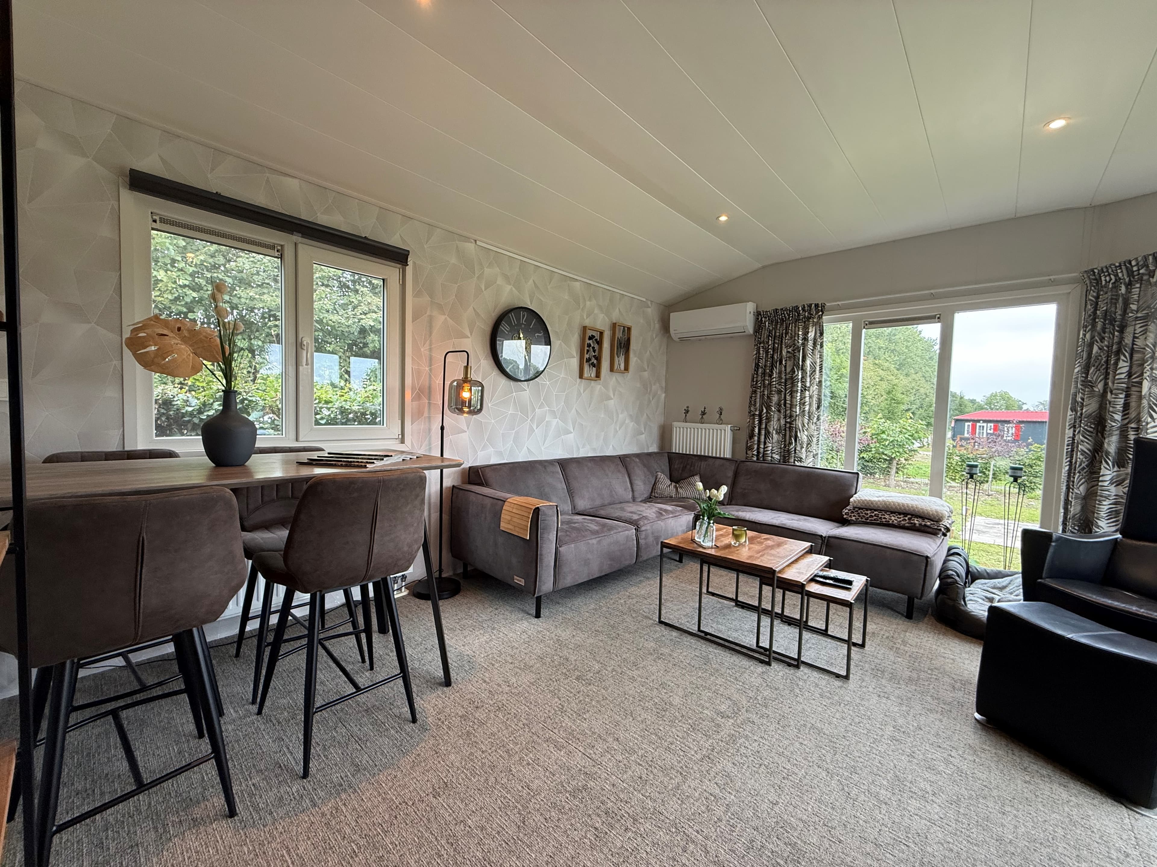 Moderne woonkamer met zithoek, eettafel en grote ramen met uitzicht op de buitenruimte.