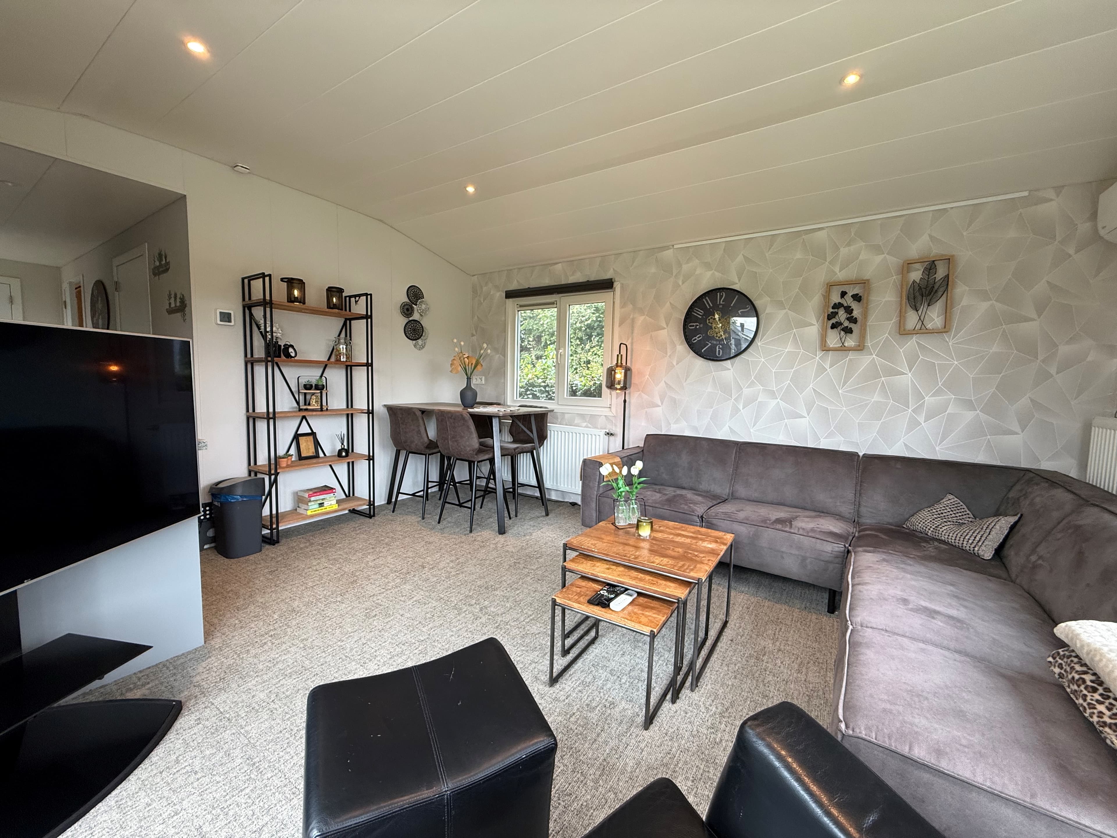 Ruime woonkamer met een zithoek, eethoek, moderne decoraties en een grote tv.