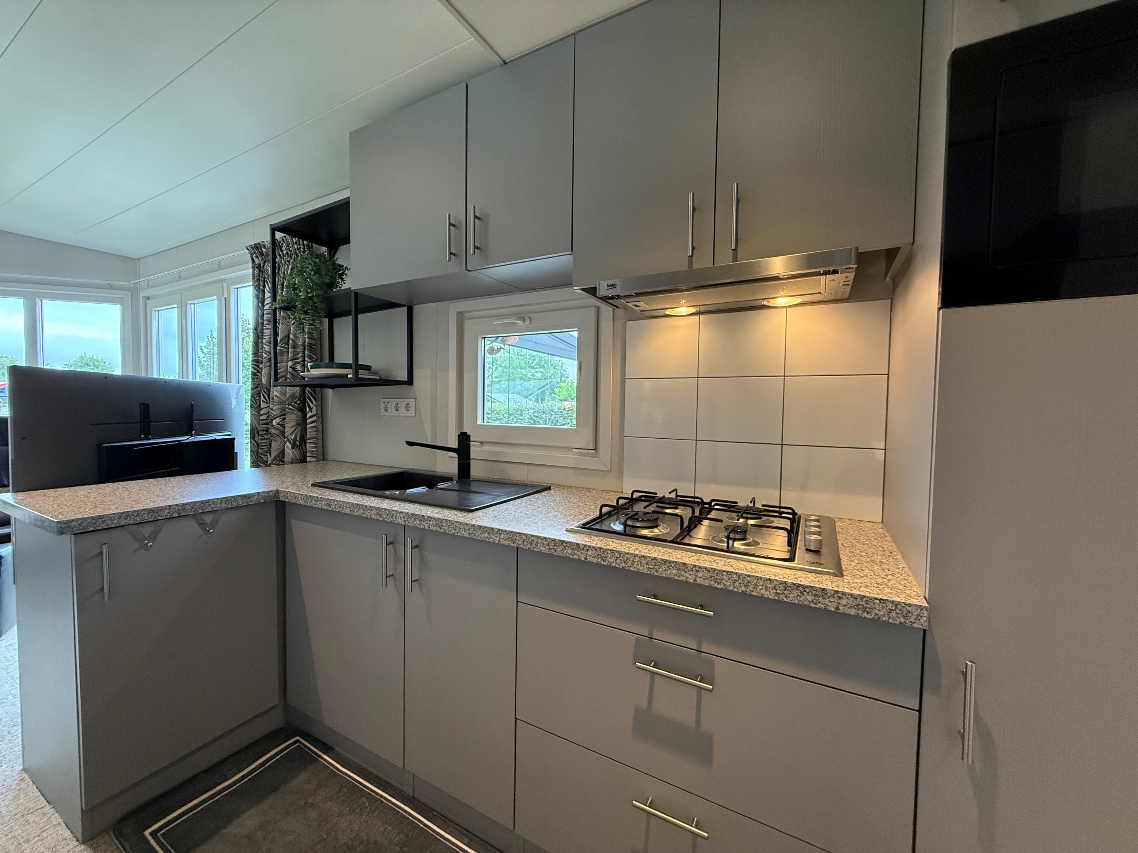 Moderne keuken met gasfornuis, spoelbak en werkblad in een vakantiewoning, veel natuurlijk licht door ramen.