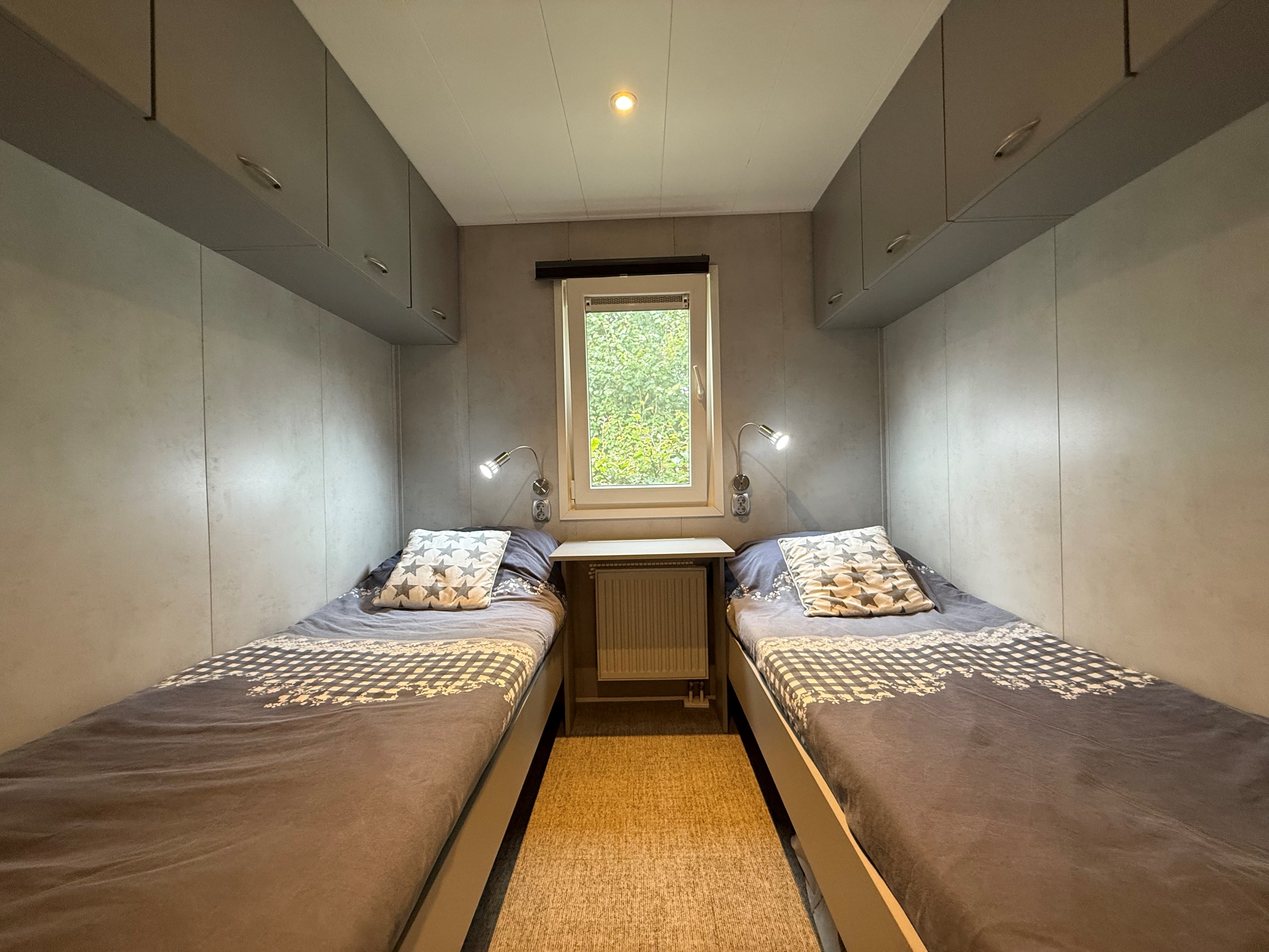 Slaapkamer met twee eenpersoonsbedden, een raam met uitzicht op bomen en wandlampen aan beide zijden.