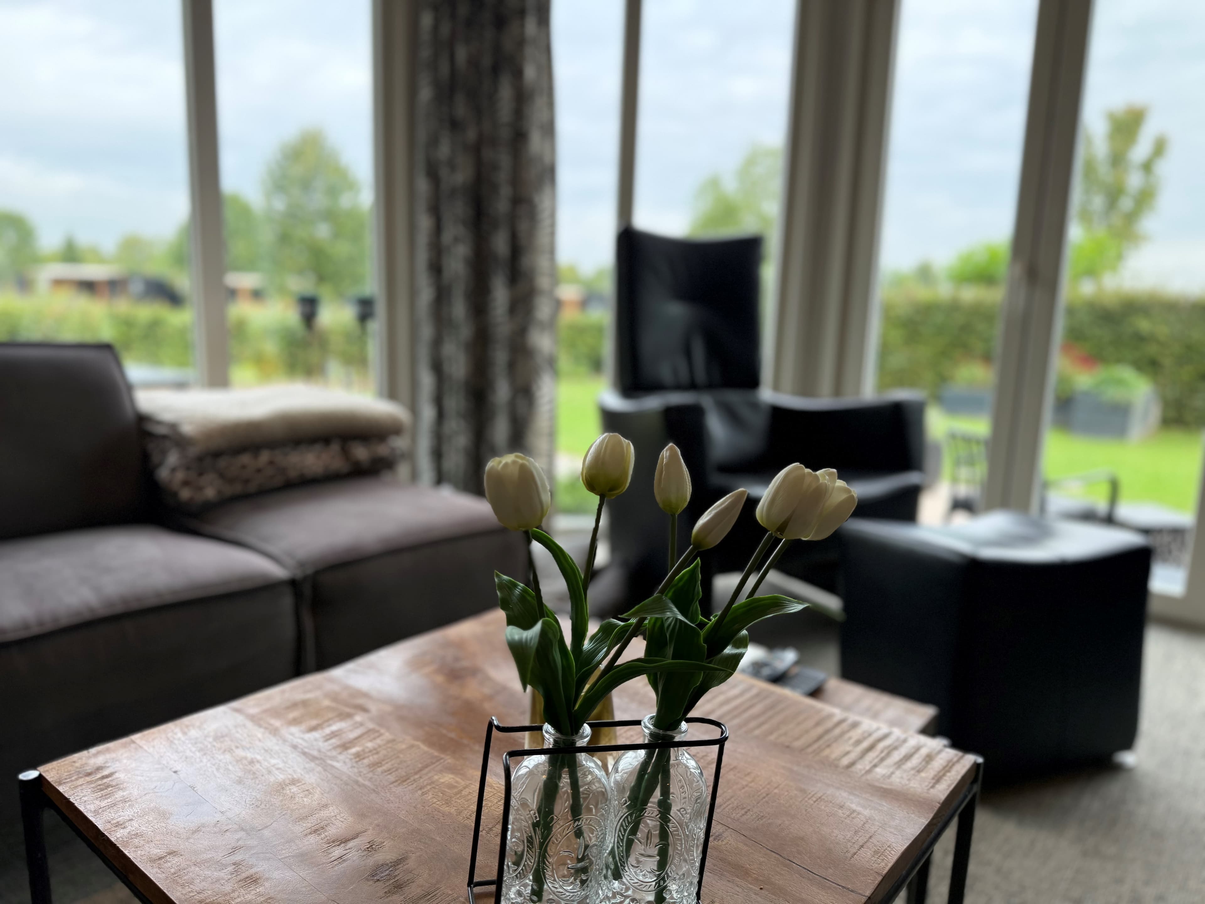 Gezellige woonkamer met een houten tafel, een vaas met tulpen en zicht op groen buitengebied door grote ramen