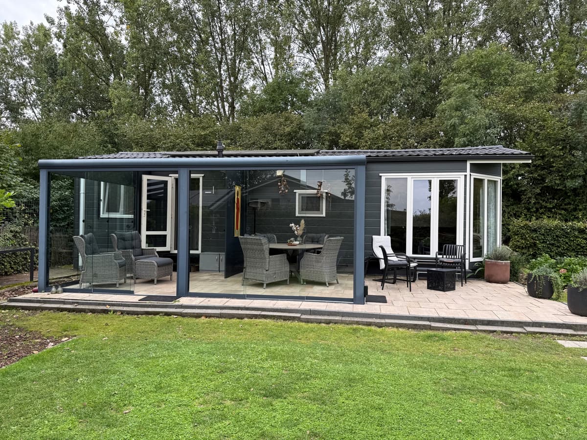 Moderne recreatiewoning met een glazen overkapping en buitenmeubilair in een groene omgeving
