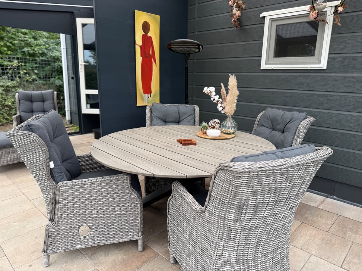 Tuinset met vier grijze stoelen rond een ronde tafel, decoratief schilderij aan de muur en planten in vaas in een overdekte r