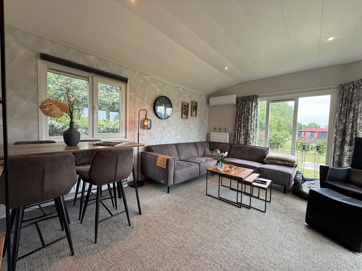Moderne woonkamer met zithoek, eettafel en grote ramen met uitzicht op de buitenruimte.