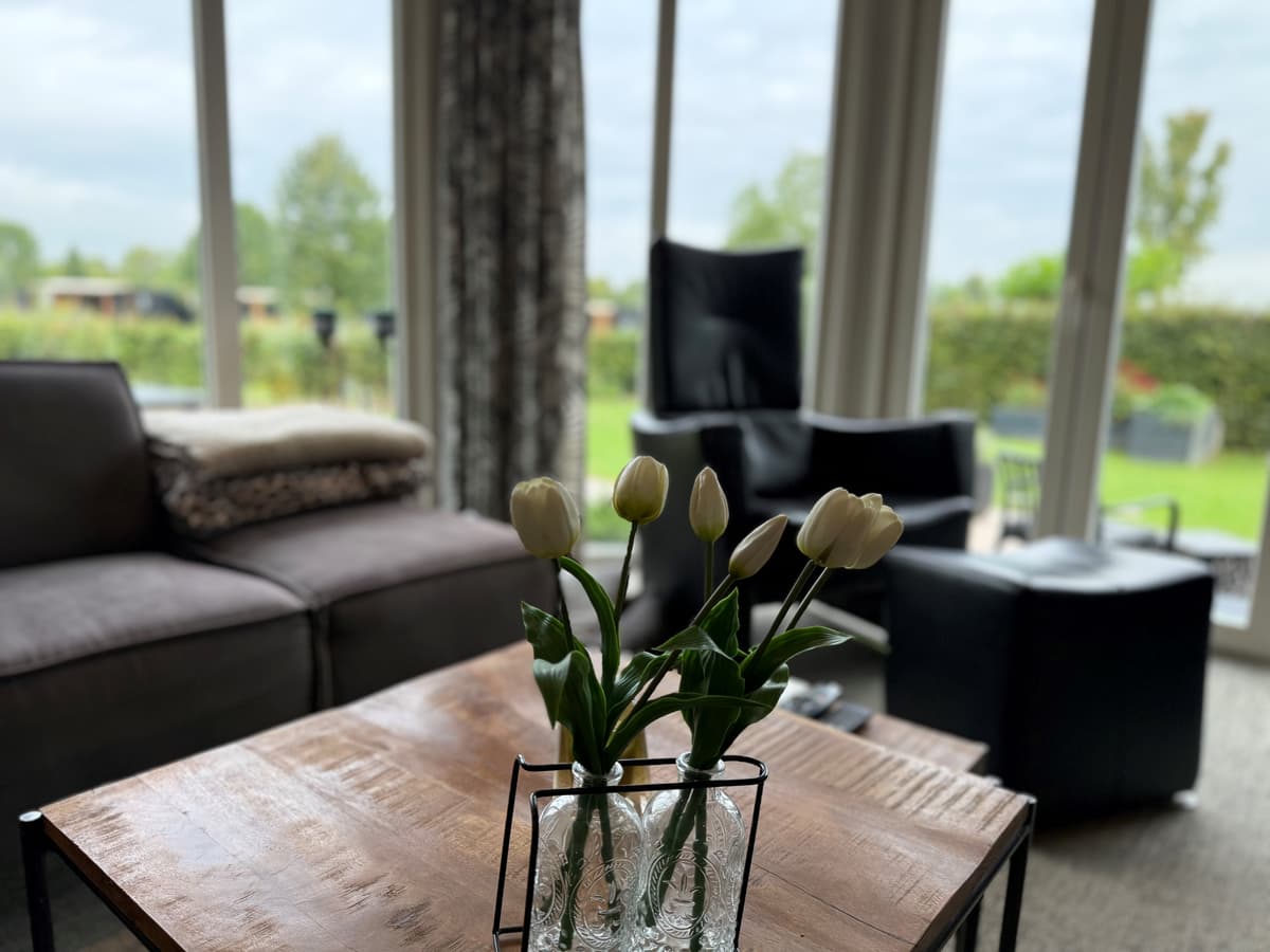 Gezellige woonkamer met een houten tafel, een vaas met tulpen en zicht op groen buitengebied door grote ramen