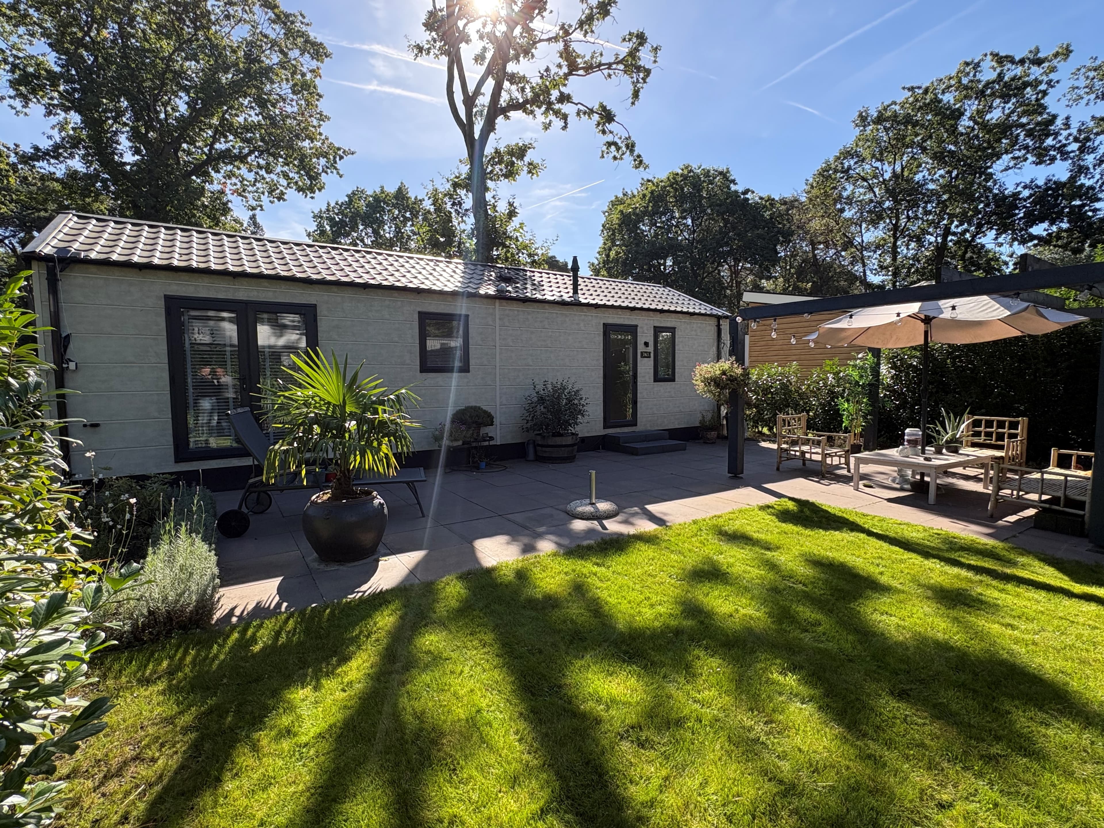 Recreatiewoning met een groene tuin, terrasschermen en zonnebloemen onder een heldere lucht in Harderwijk.