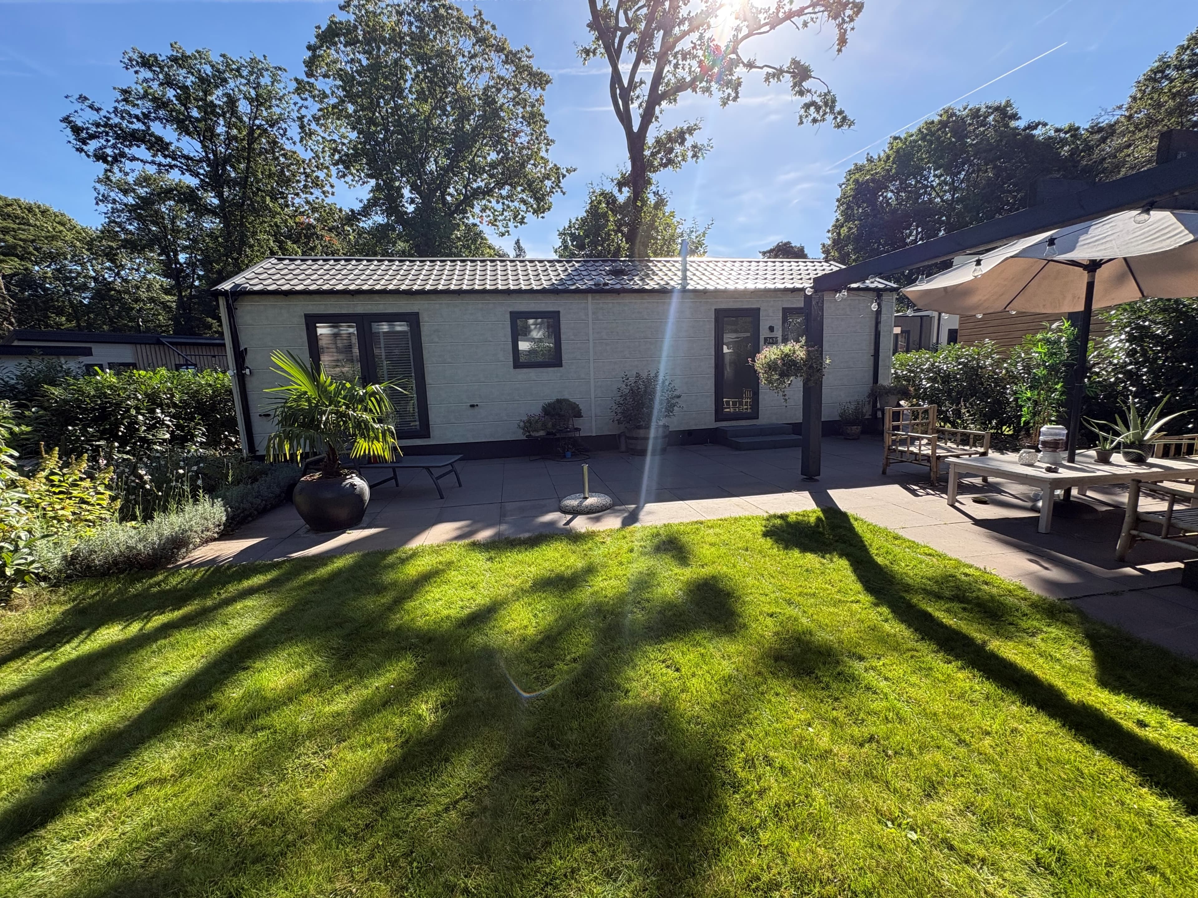 Recreatiewoning met tuin, terras en parasol, omgeven door gras en bomen op Camping De Konijnenberg in Harderwijk