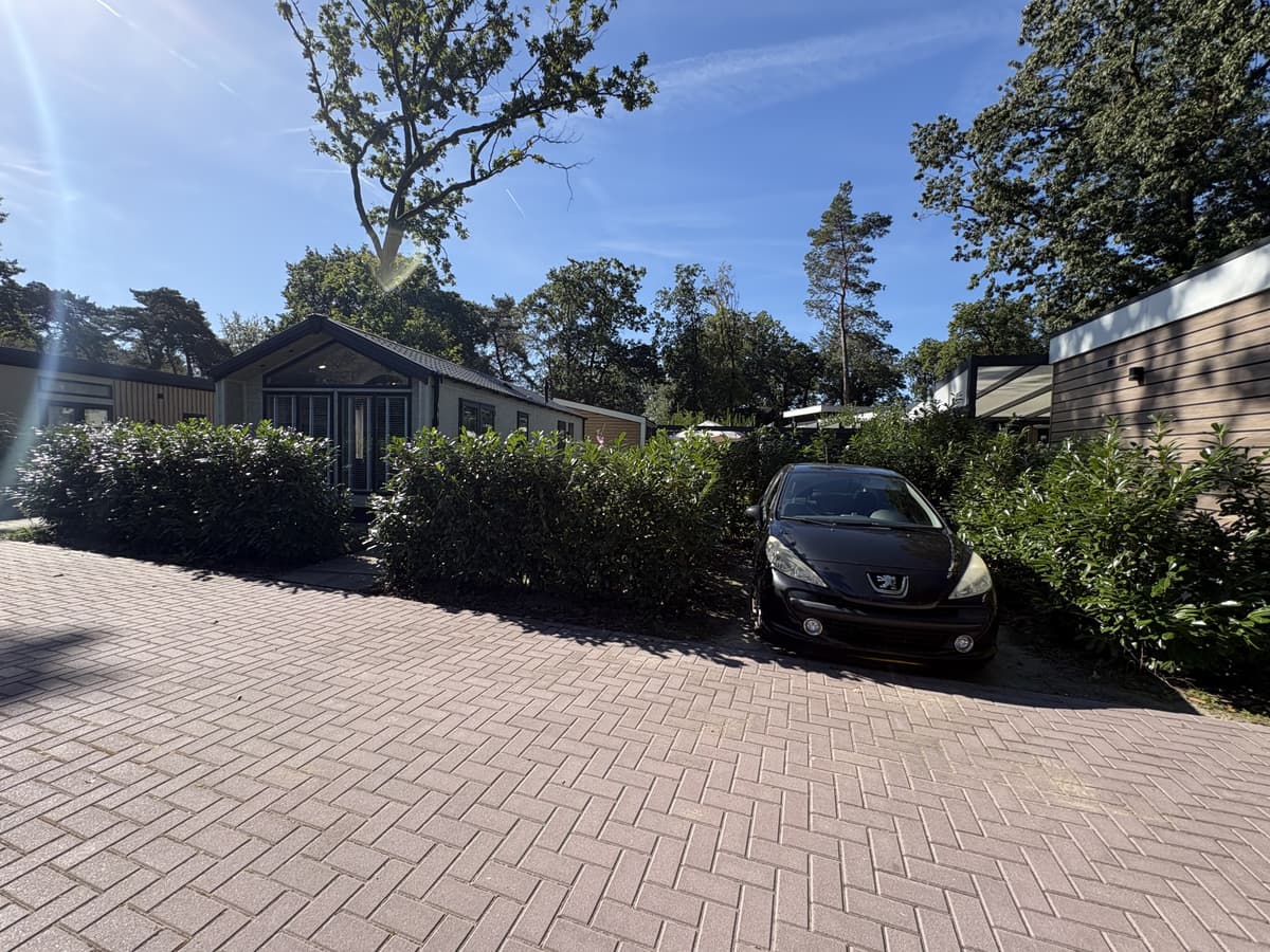 Recreatiewoning met voortuin en parkeermogelijkheid voor een auto, omringd door groene heggen en bomen