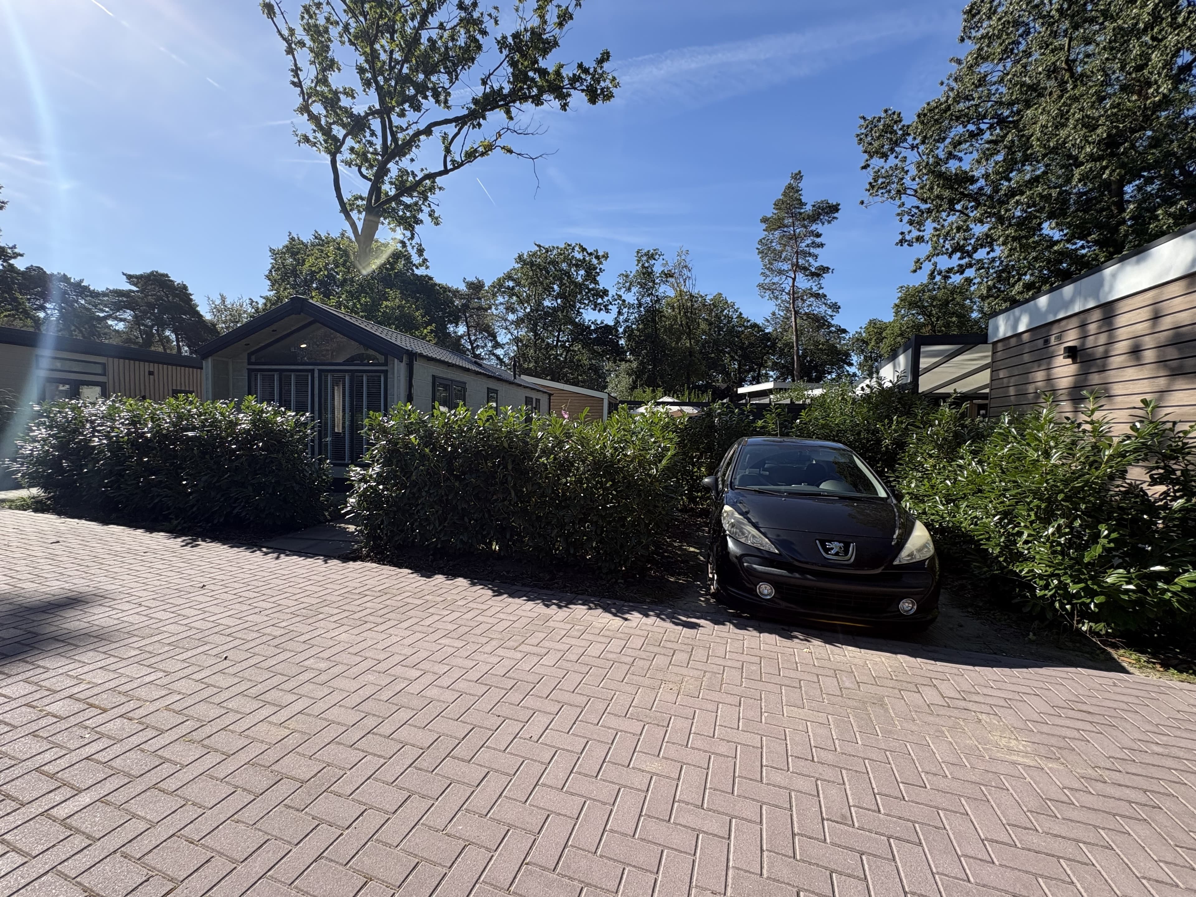 Recreatiewoning met voortuin en parkeermogelijkheid voor een auto, omringd door groene heggen en bomen