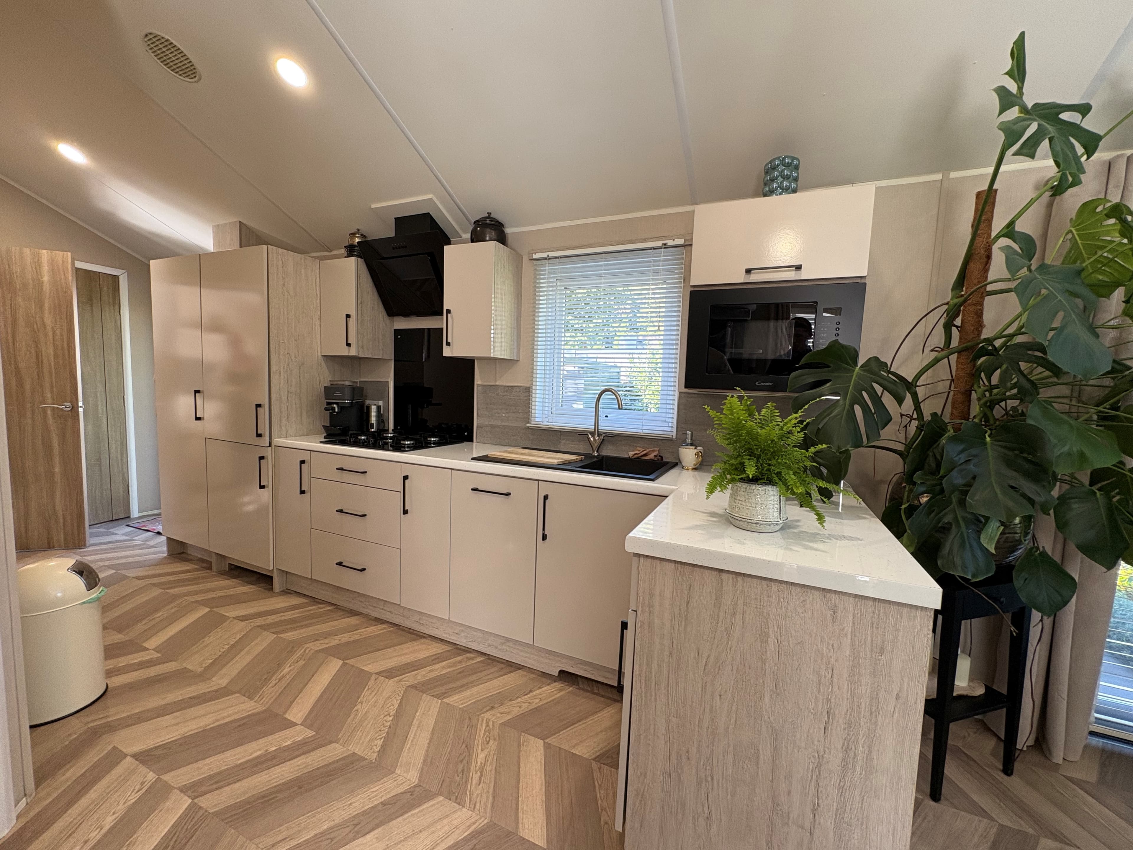 Moderne keuken met lichtgekleurde kasten, inbouwapparatuur en een plantenbak, gesitueerd in een recreatiewoning.