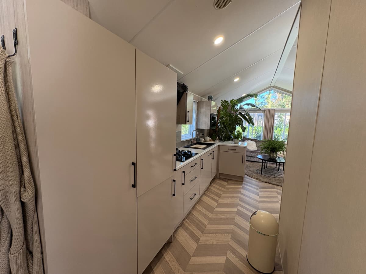 Keuken in recreatiewoning met moderne kasten, gasfornuis en een grote plant bij een raam voor natuurlijk licht