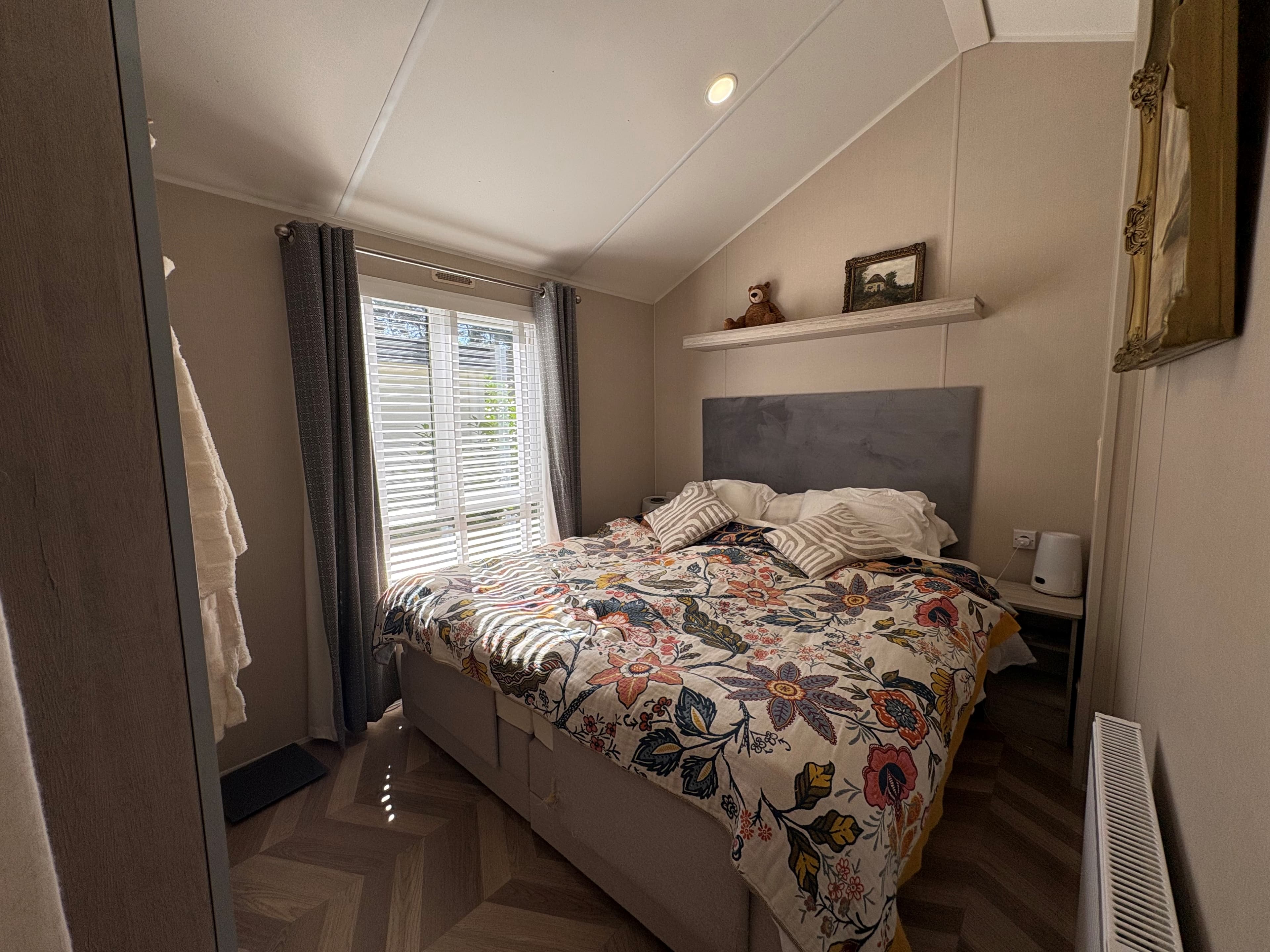 Slaapkamer met een tweepersoonsbed, kleurrijk dekbedovertrek en lichtinval via houten jaloezieën.