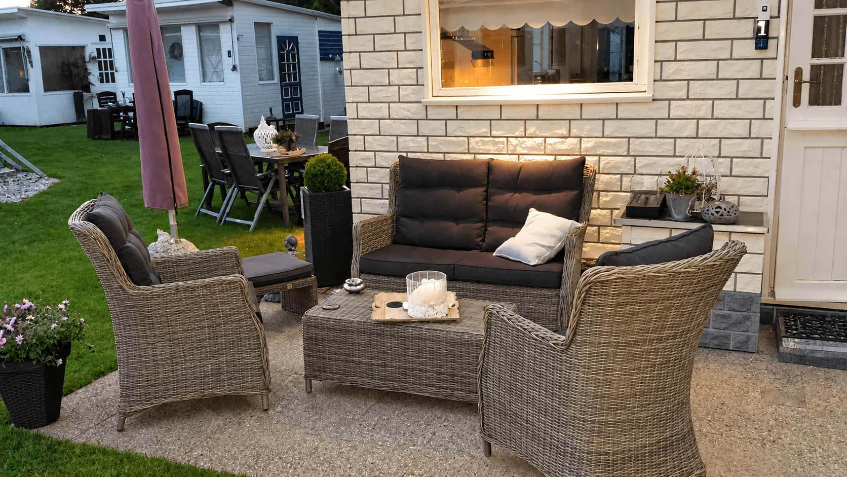 Terras met een rieten meubelset, waaronder een bank en stoelen, met planten en een tafel in een groene omgeving