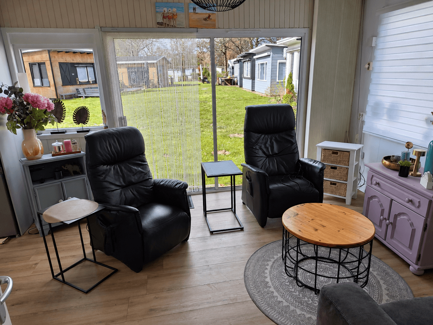 Zithoek met twee zwarte twill-stoelen, bijzettafels en een houten salontafel, met uitzicht op een groene tuin buiten.