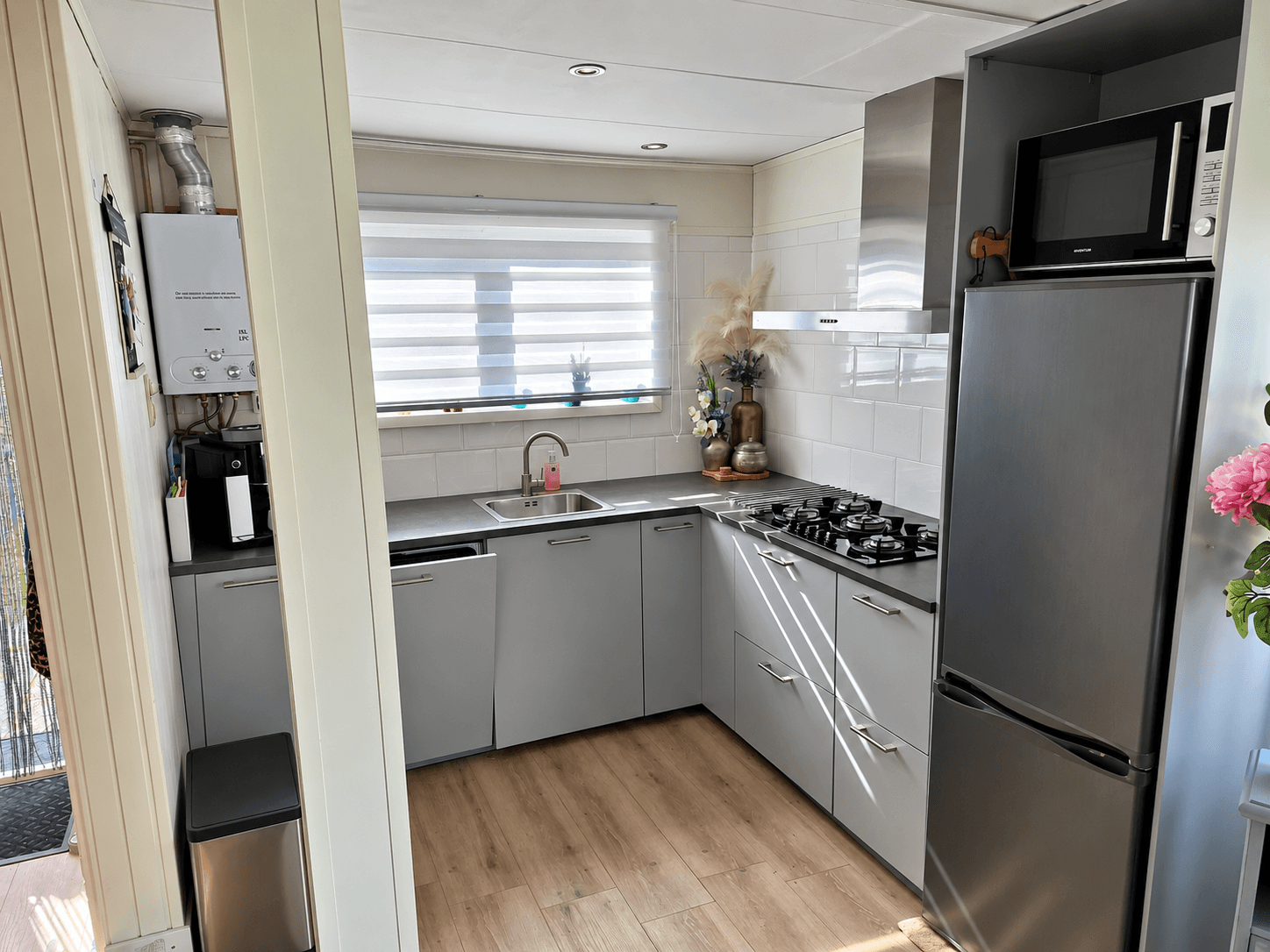Moderne keuken met grijze kasten, gasfornuis, spoelbak en koelkast, voorzien van natuurlijk licht en houten vloer