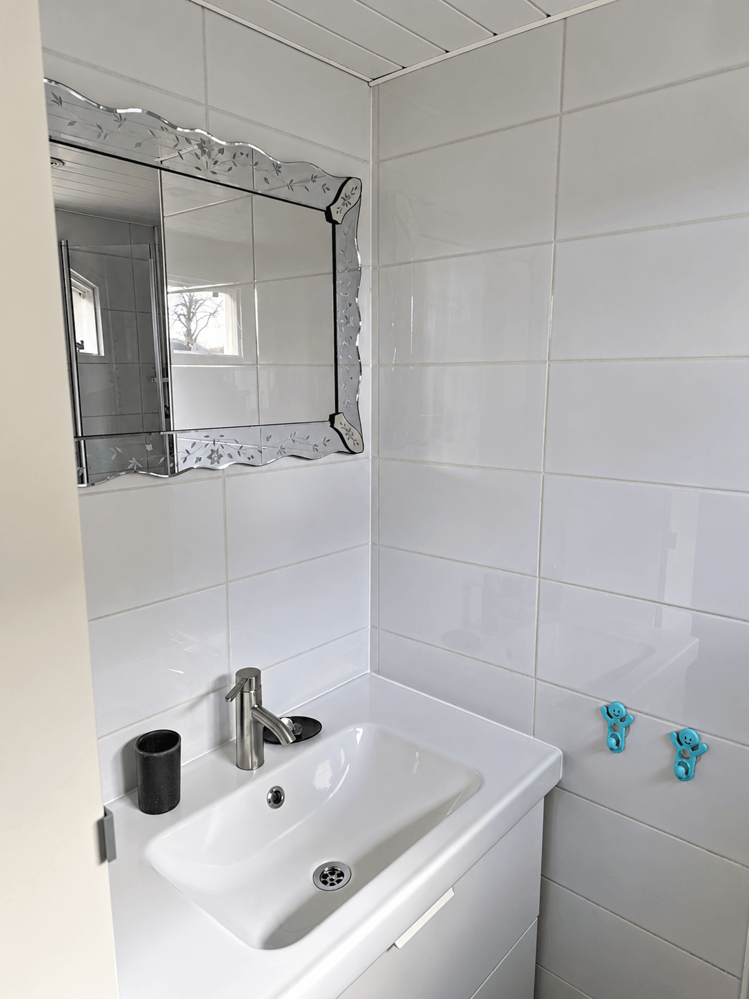 Badkamer met een wastafel, spiegel, en tegels in lichte kleuren, met een waterkraan en geen zichtbare douche of bad.