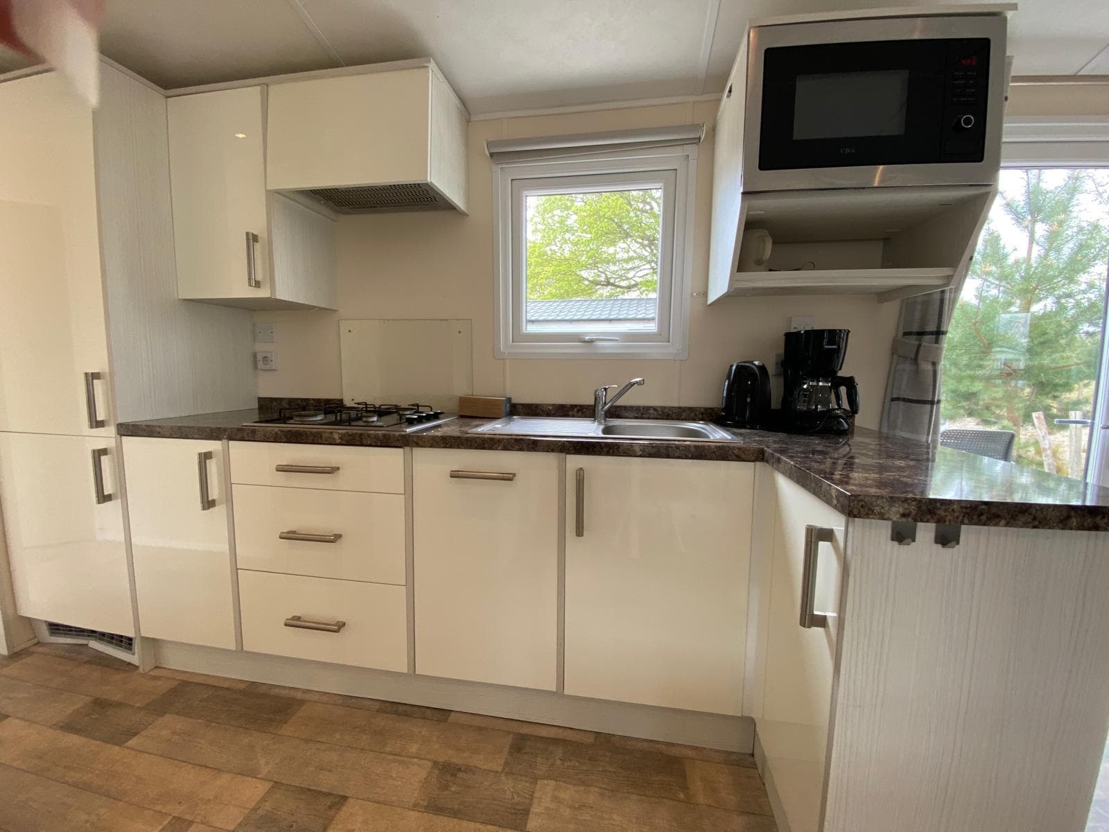 Moderne keuken met witte kasten, gasfornuis, afwasbak en een microwave, zichtbaar vanuit een hoek.