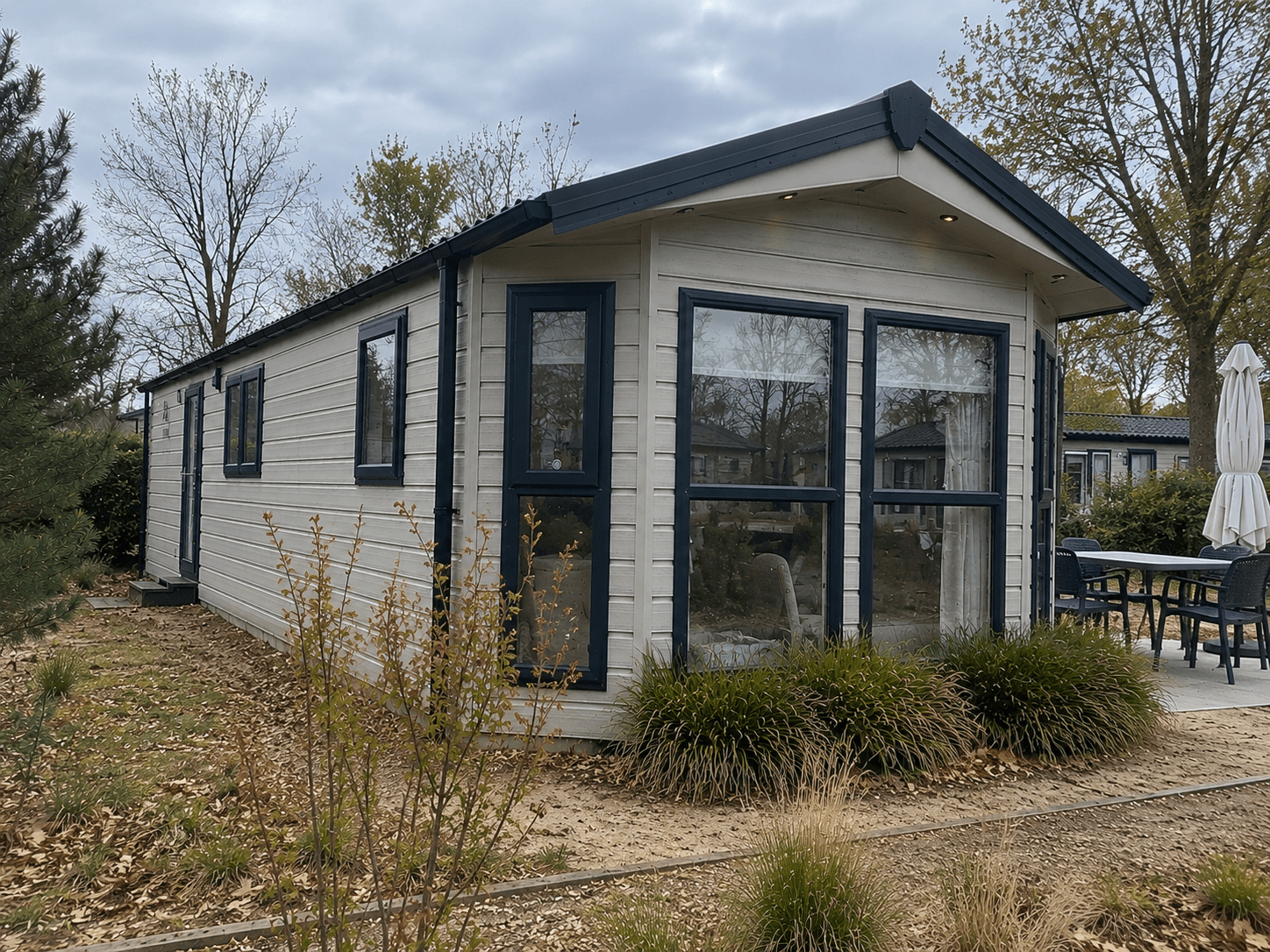 Moderne recreatiewoning met grote ramen, omgeven door groen en een terras met tuinmeubilair.