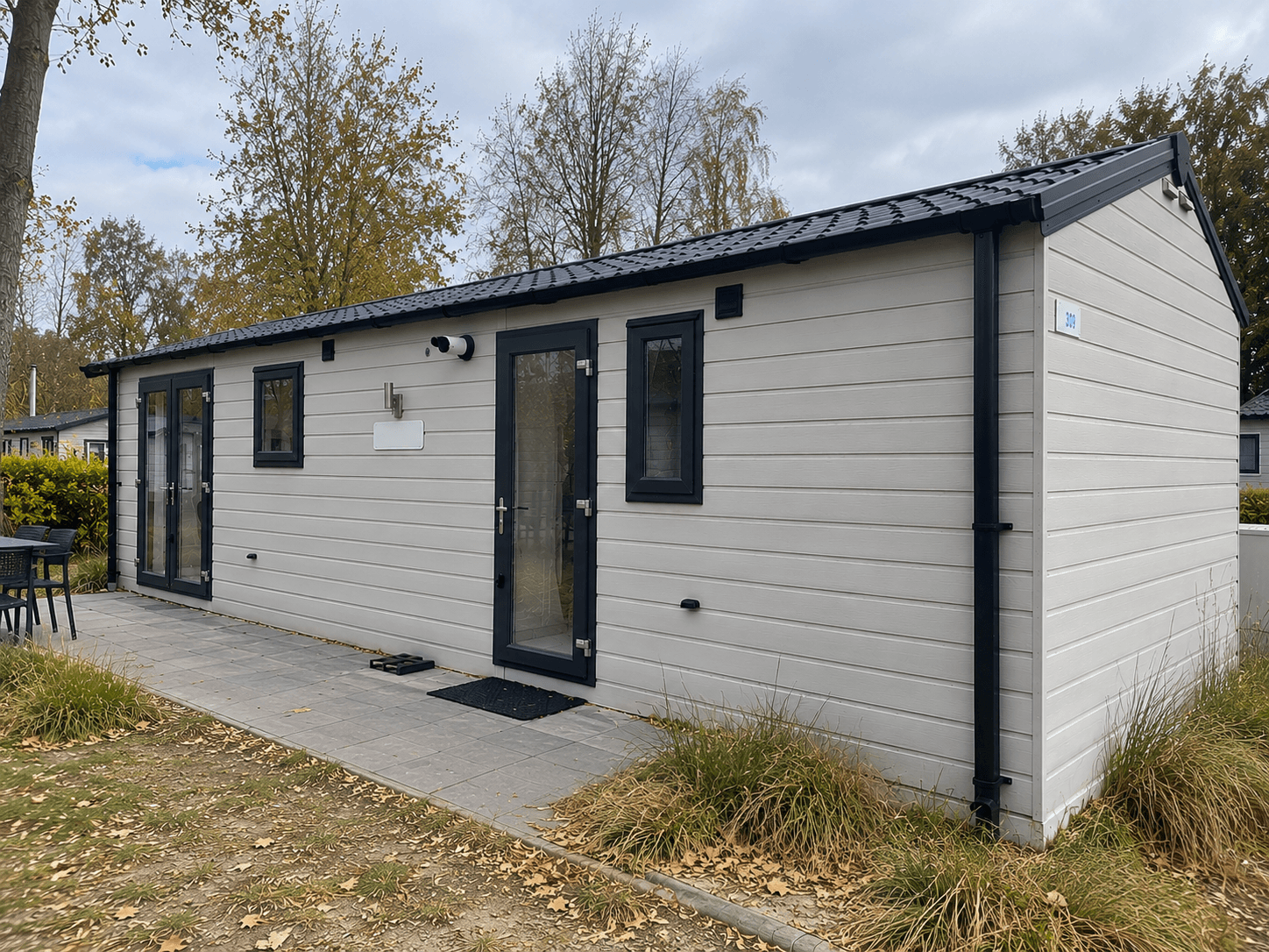 Moderne recreatiewoning met lichte gevel, grote ramen en een terras van tegels in een groene omgeving