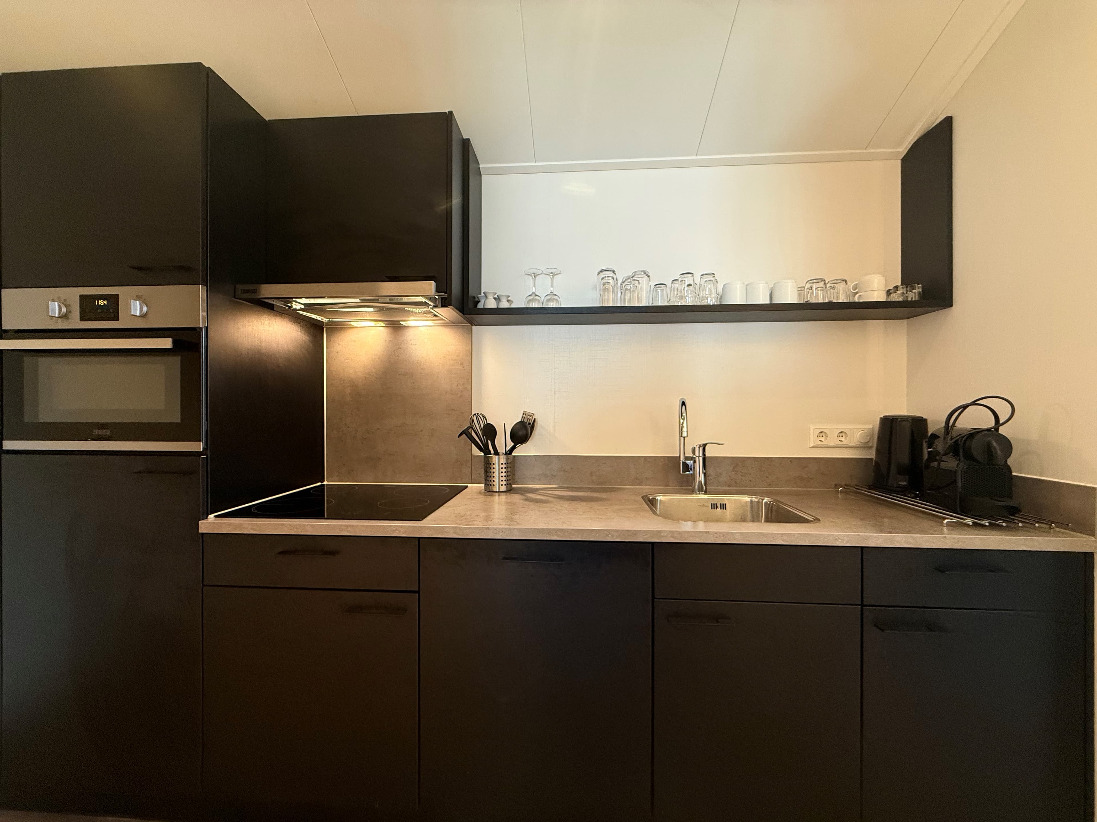 Moderne keuken met zwarte kasten, ingebouwde oven, inductiekookplaat en aanrecht met spoelbak en keukenapparatuur