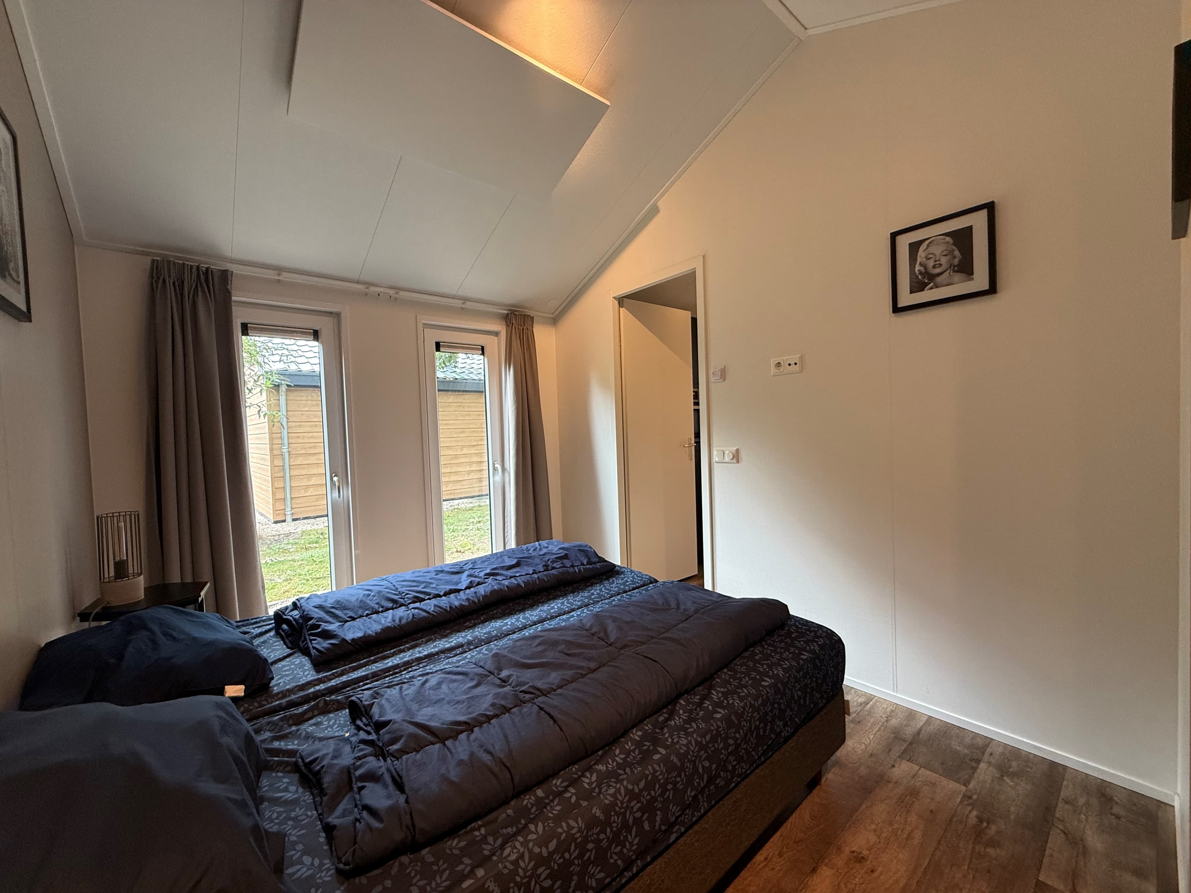 Slaapkamer met twee bedden, raam met uitzicht op een tuin en een deur naar buiten, lichte muren en vloer.