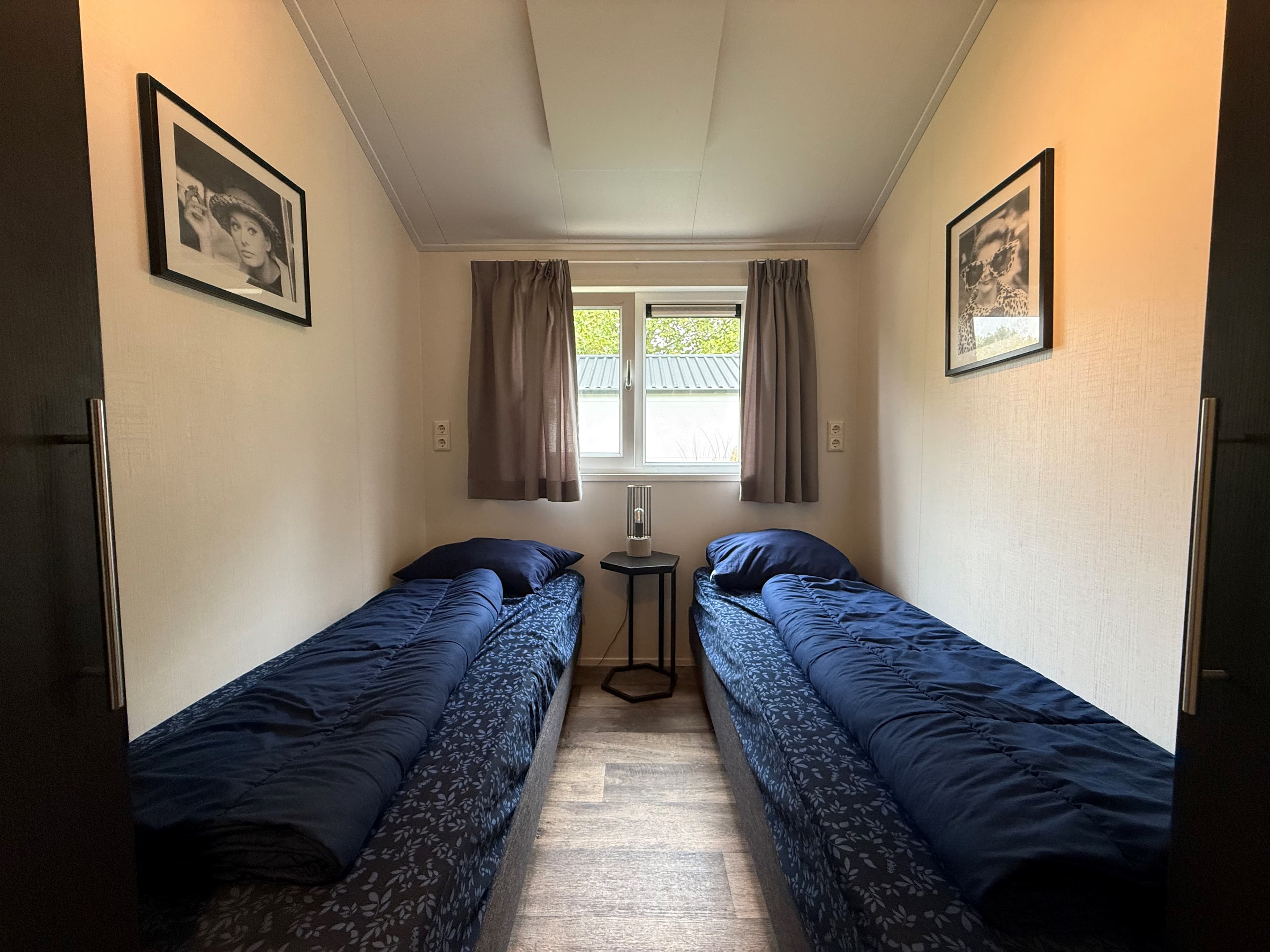 Sfeervolle slaapkamer met twee éénpersoonsbedden, raam met gordijnen en foto's aan de muur.