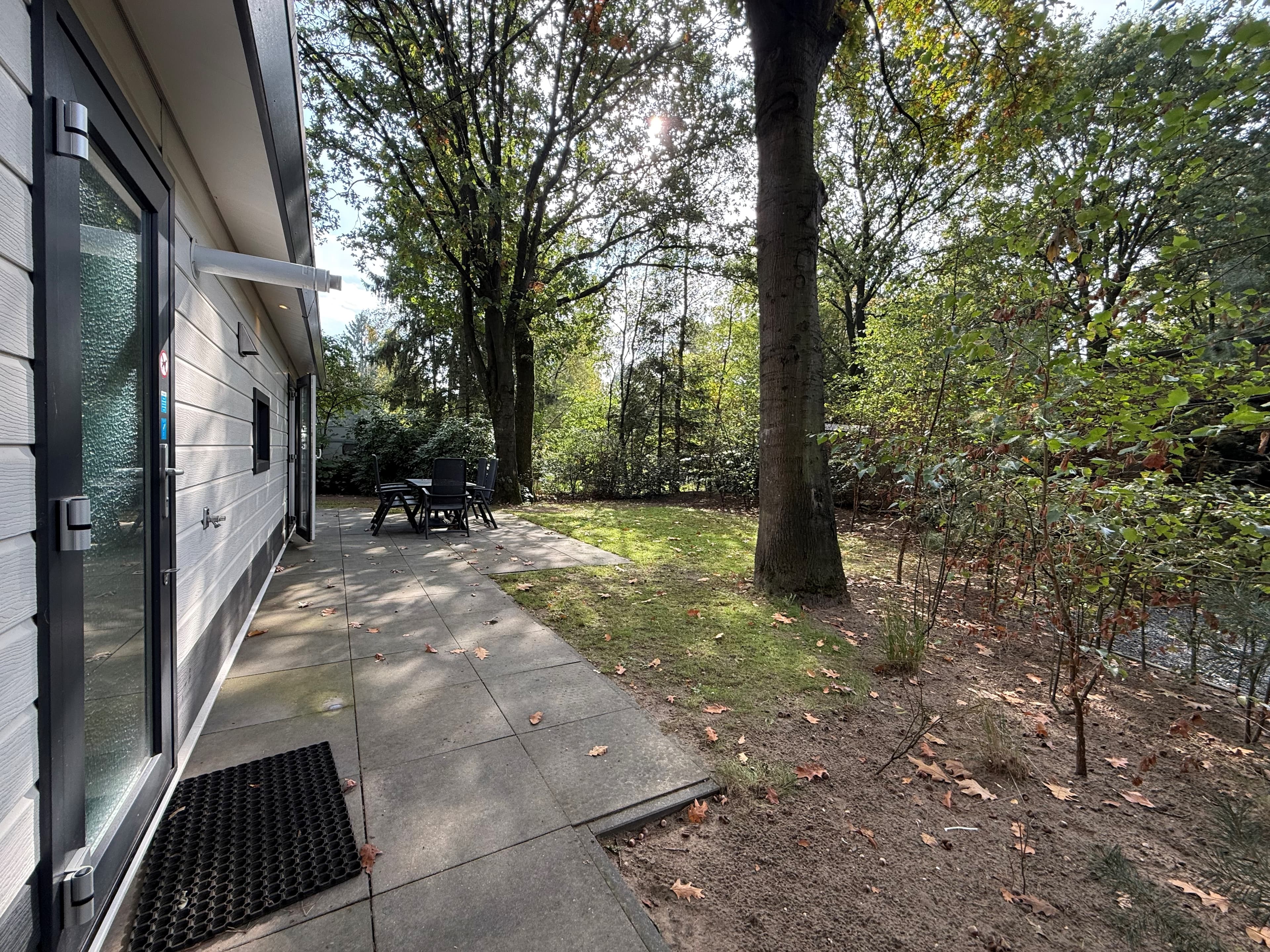 Terras met tuinmeubilair en groen aan de zijkant van de recreatiewoning omringd door bomen en struiken