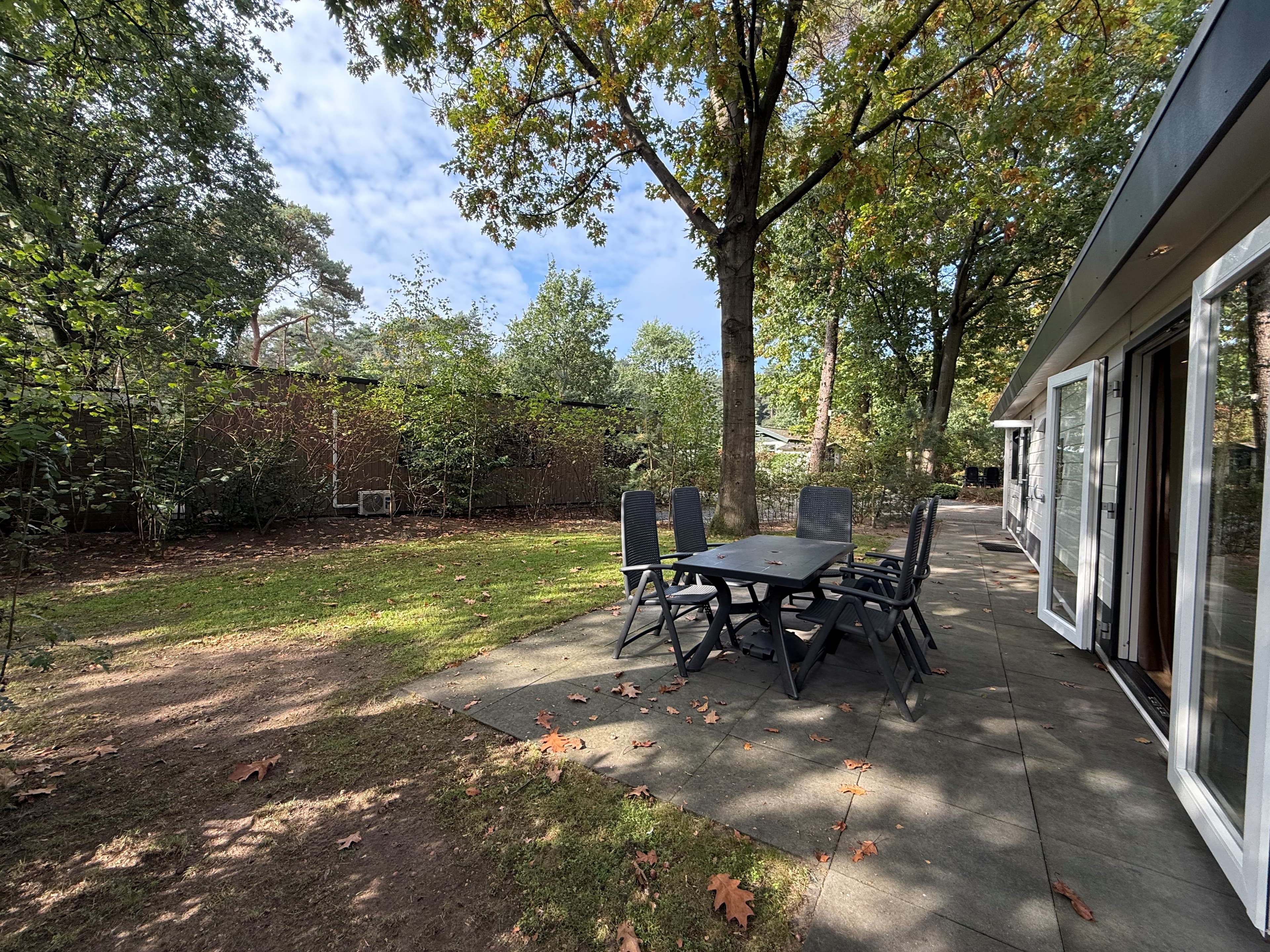 Terras met een tafel en stoelen, omringd door groen, zicht op ruimte met bomen en gras rondom de recreatiewoning
